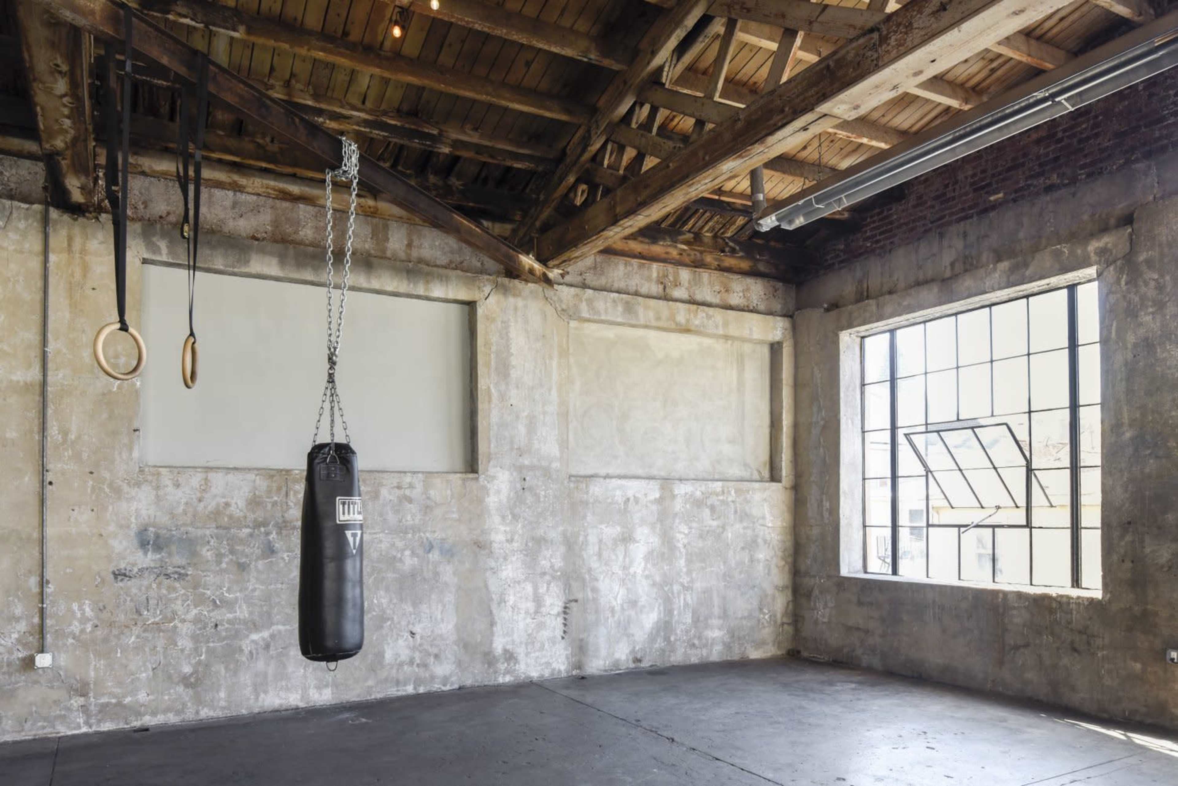 An empty gym with a boxing bag hanging from the ceiling and wooden beams exposed in the ceiling, featuring large windows that provide natural light.