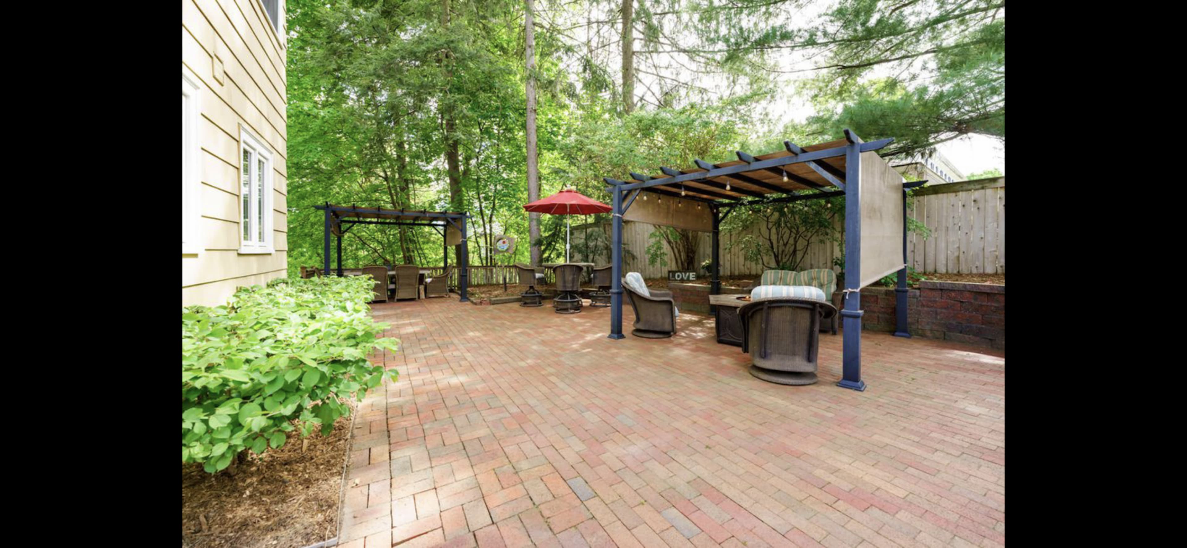A brick patio with seating areas covered by pergolas surrounded by greenery.