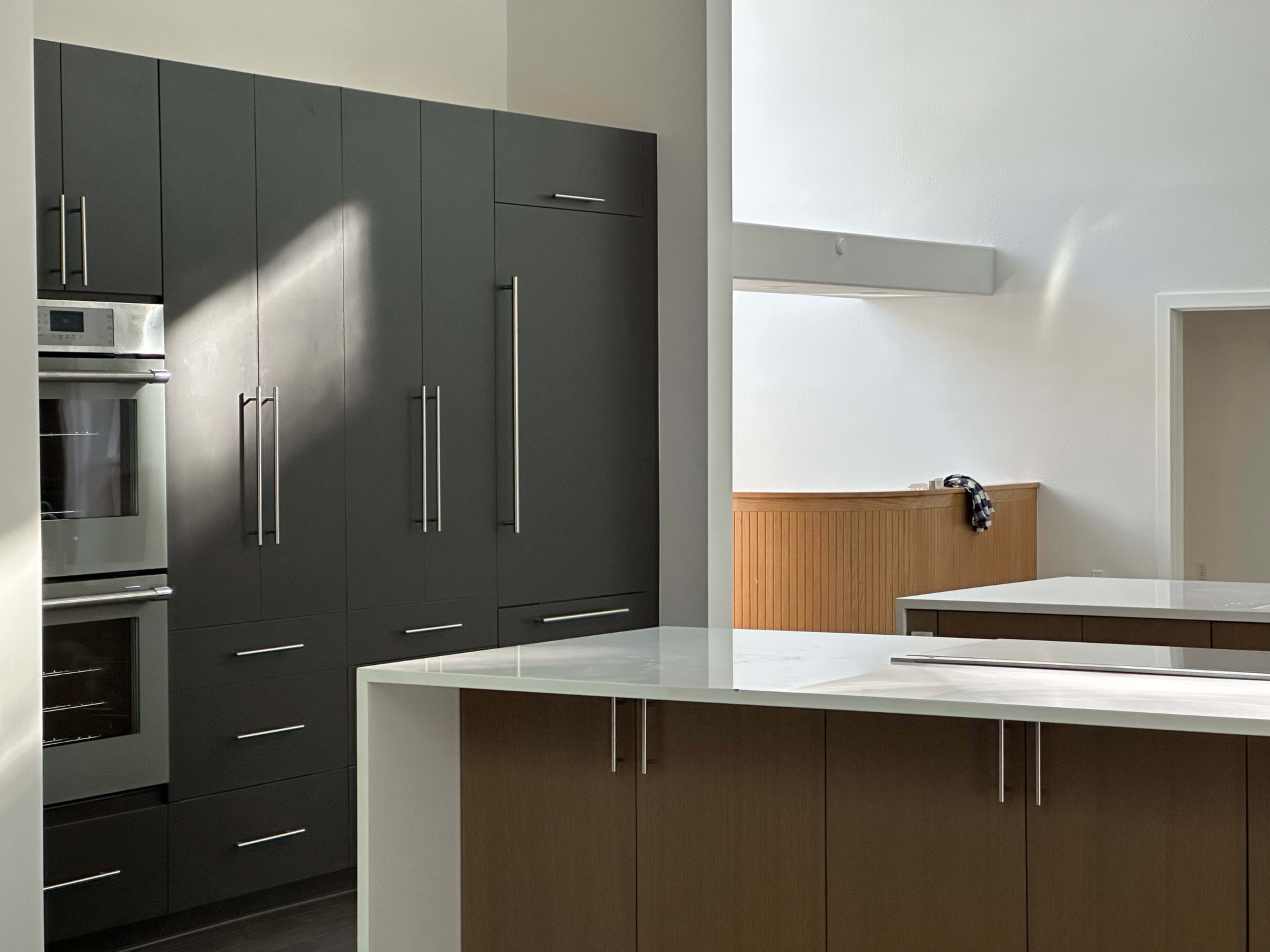 The image shows a modern kitchen with dark cabinetry, stainless steel appliances, and a white countertop.