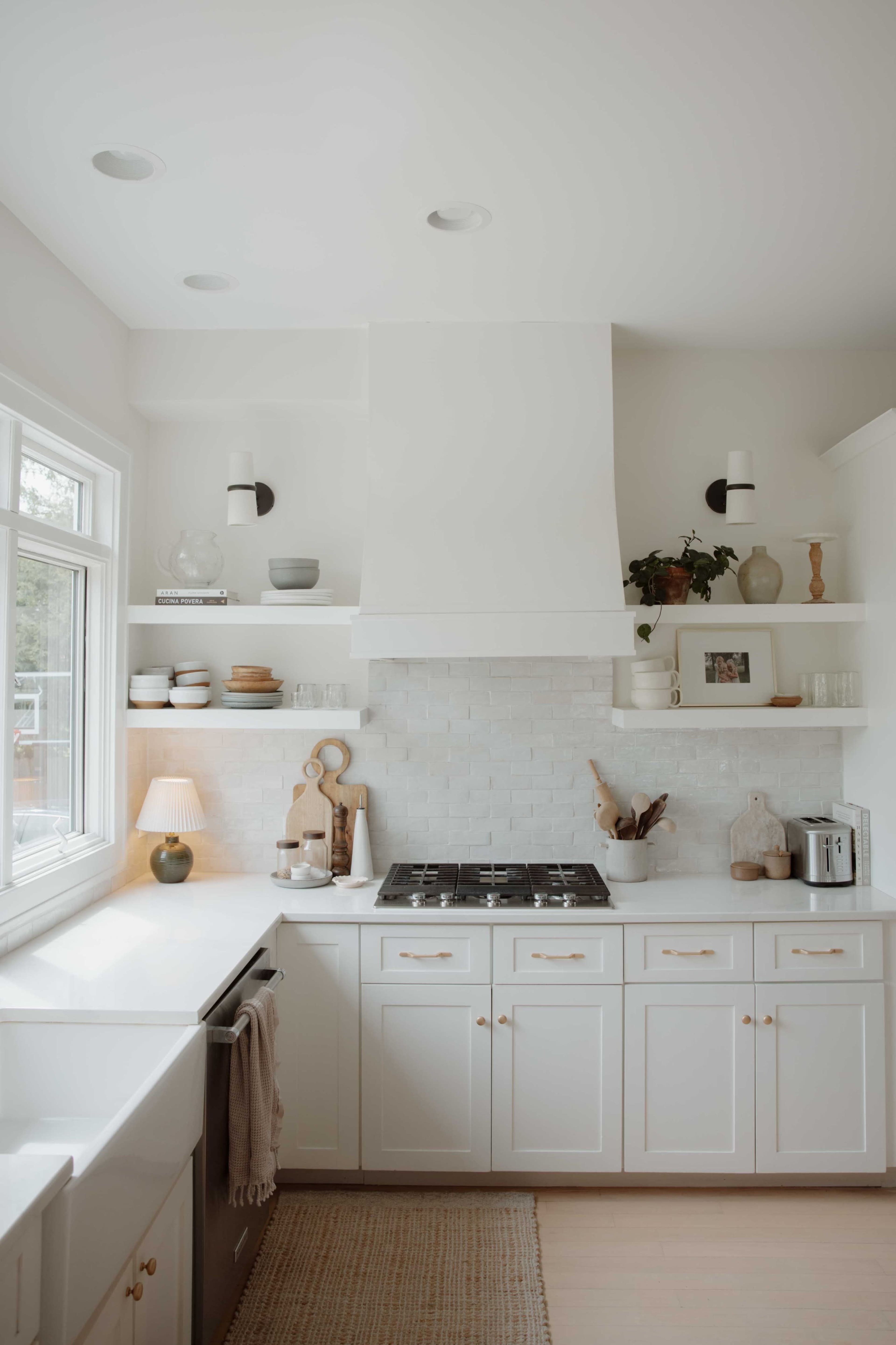 The kitchen features white cabinetry, a central island, and a tiled backsplash with a gas stovetop beneath a modern hood.
