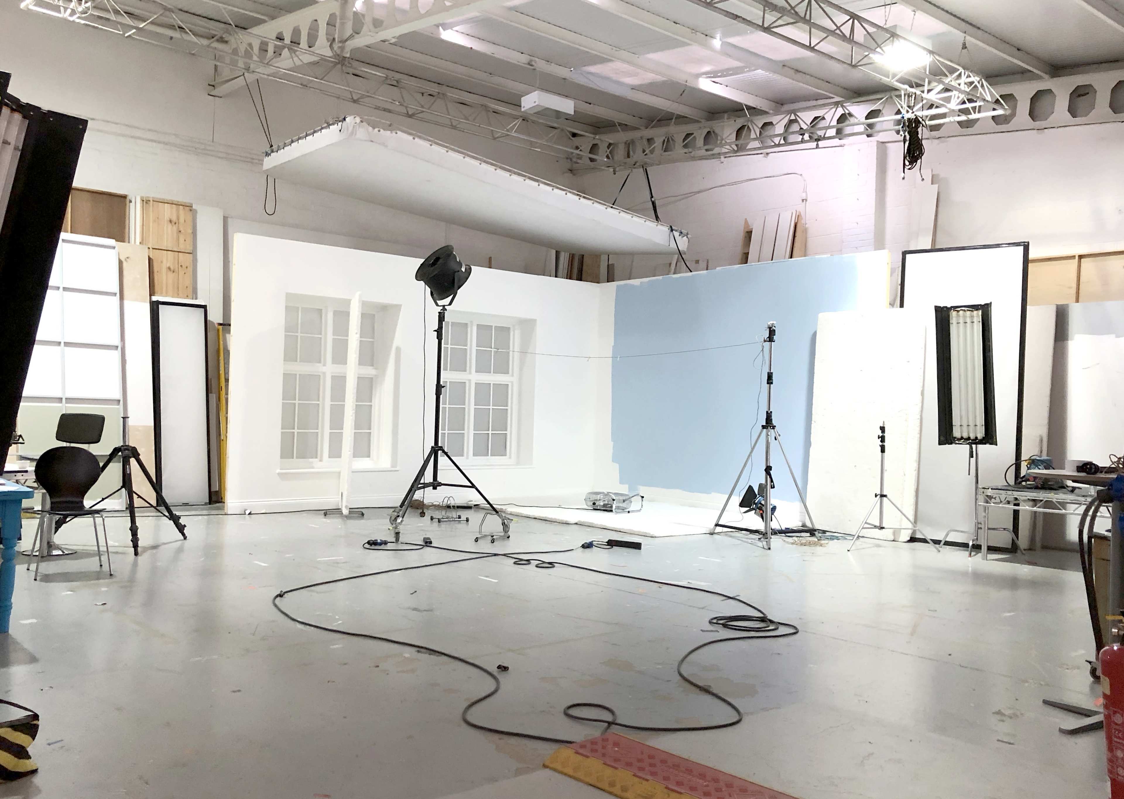 A photography studio with a white backdrop, lighting equipment, and various props scattered across the floor.