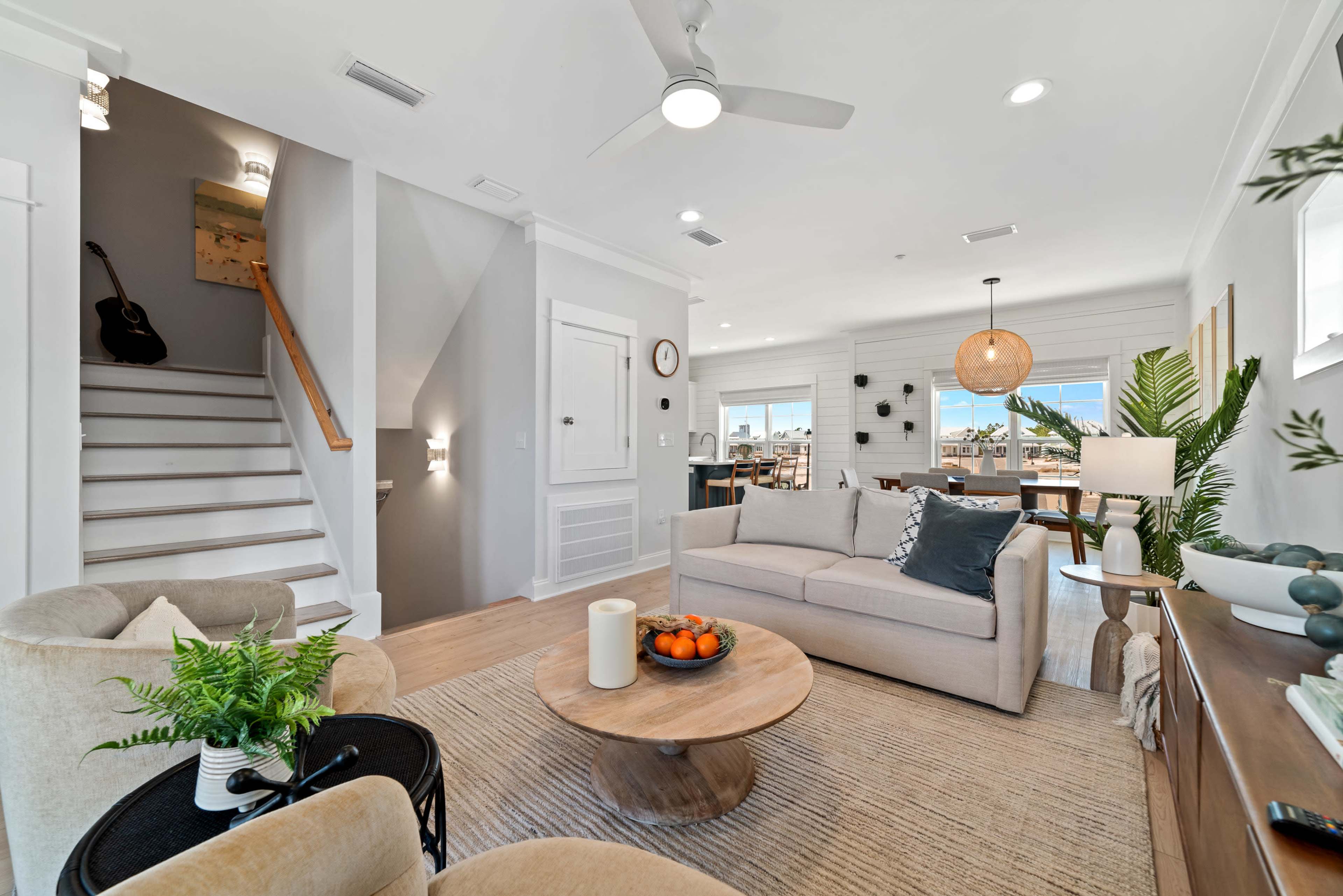 The living space features a light-filled area with a sofa, coffee table, and plants, alongside a staircase leading to the upper floor.
