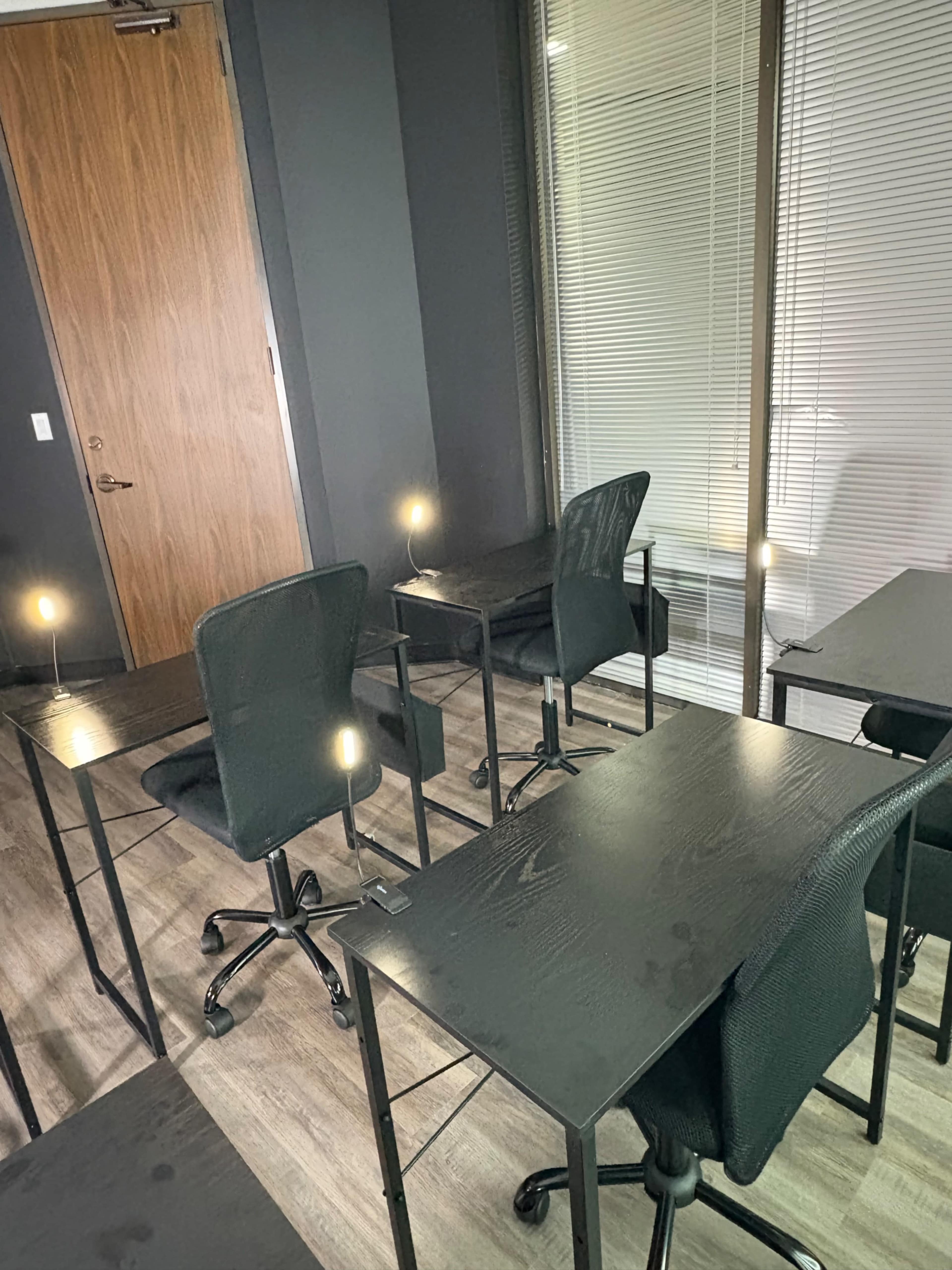 The image shows a room with several black desks and chairs arranged sparsely, illuminated by small lights.