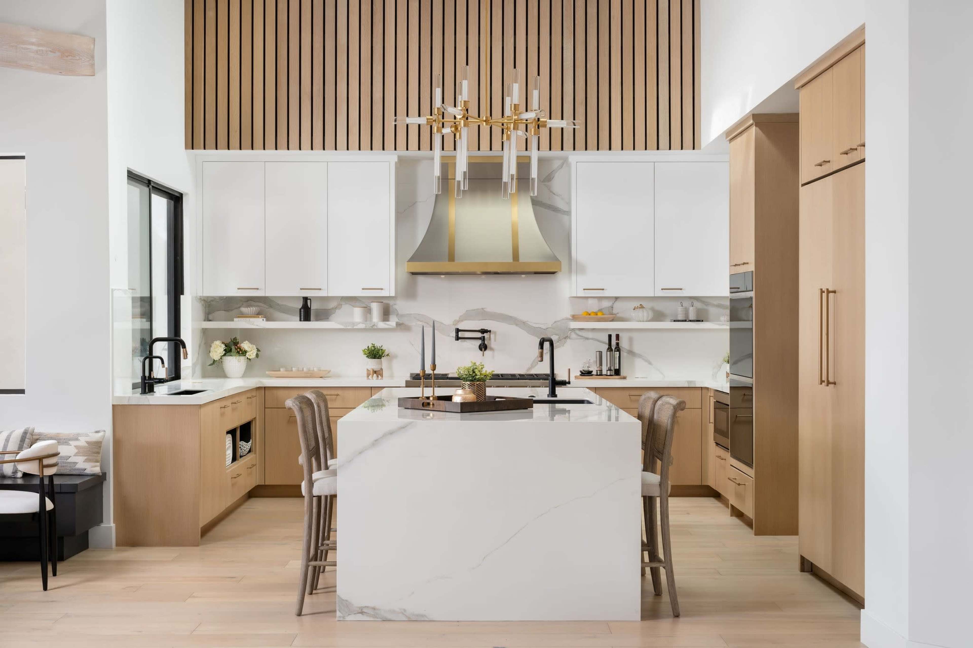 The kitchen features a large island with a marble countertop, wooden cabinetry, and modern appliances under a stylish light fixture.