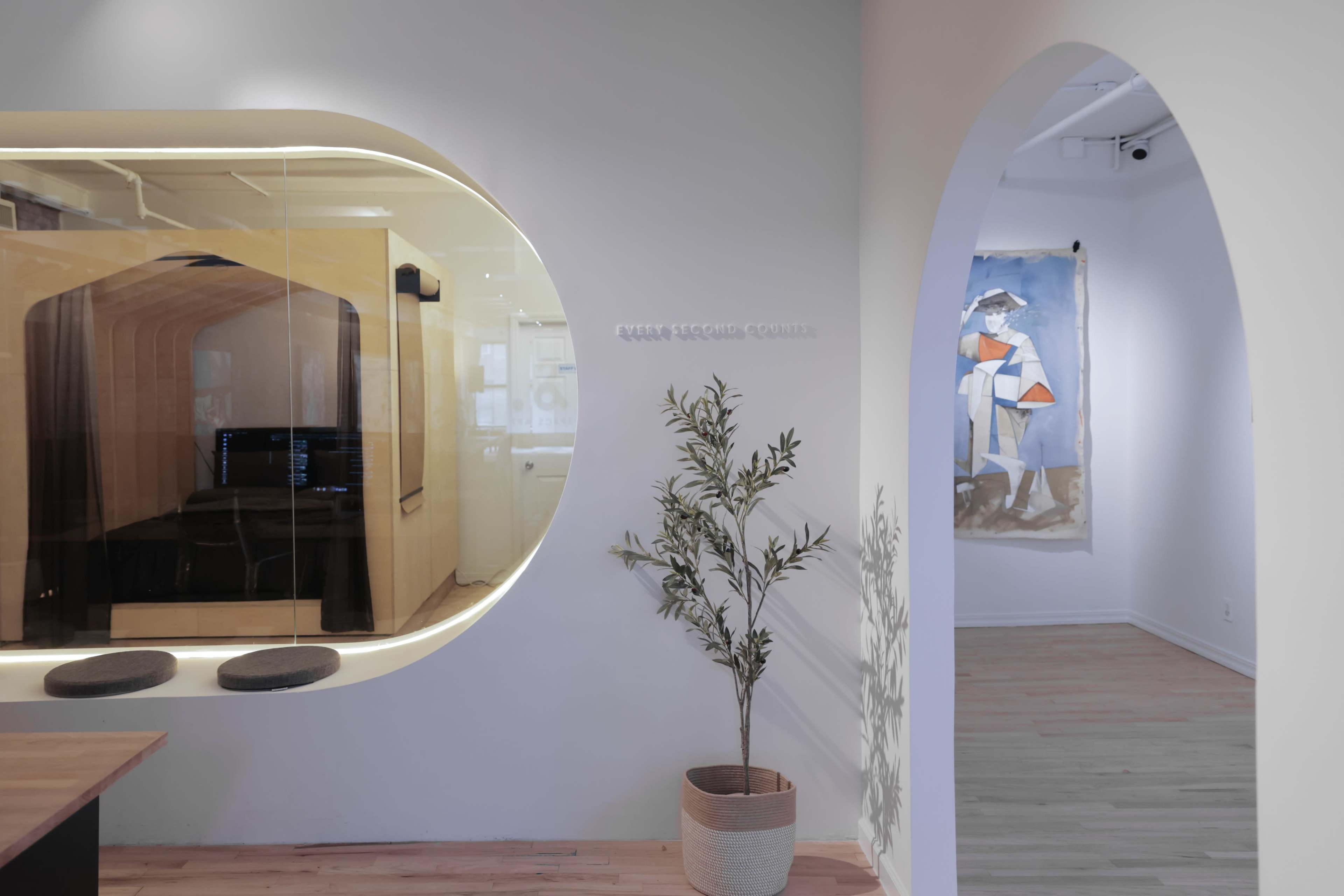 The image shows a modern office interior with a curved glass meeting room, a potted plant, and an adjacent art piece on the wall.