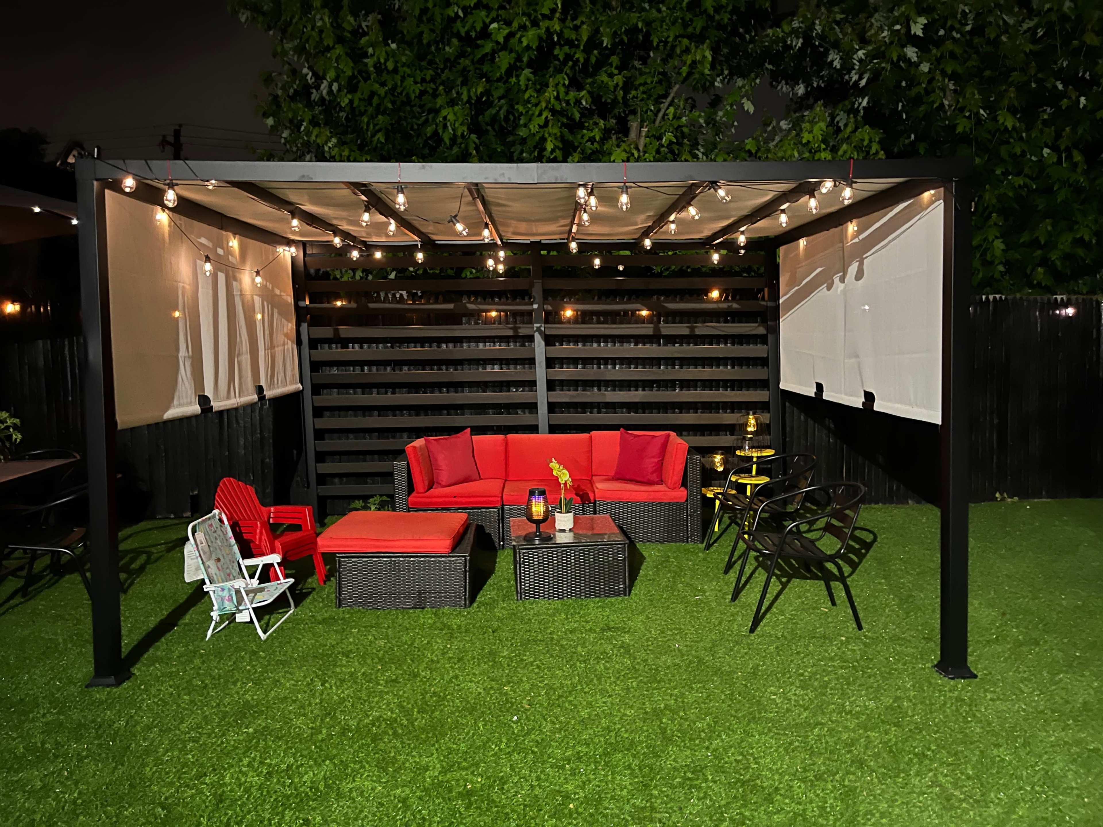 A covered outdoor seating area features red furniture, string lights, and a green artificial lawn.