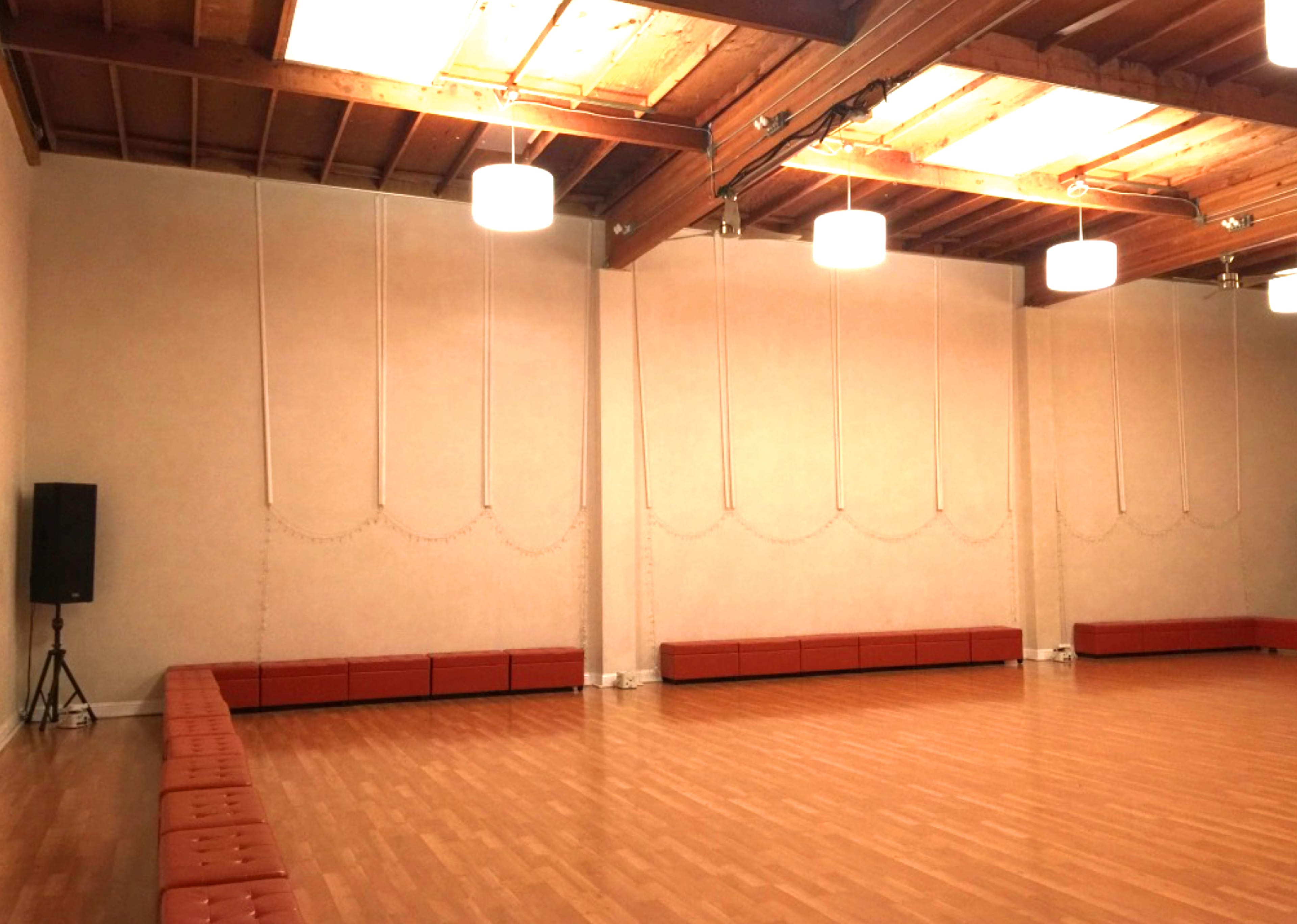 A spacious indoor room with wooden floors, wall-mounted lights, and a long padded bench along one wall.
