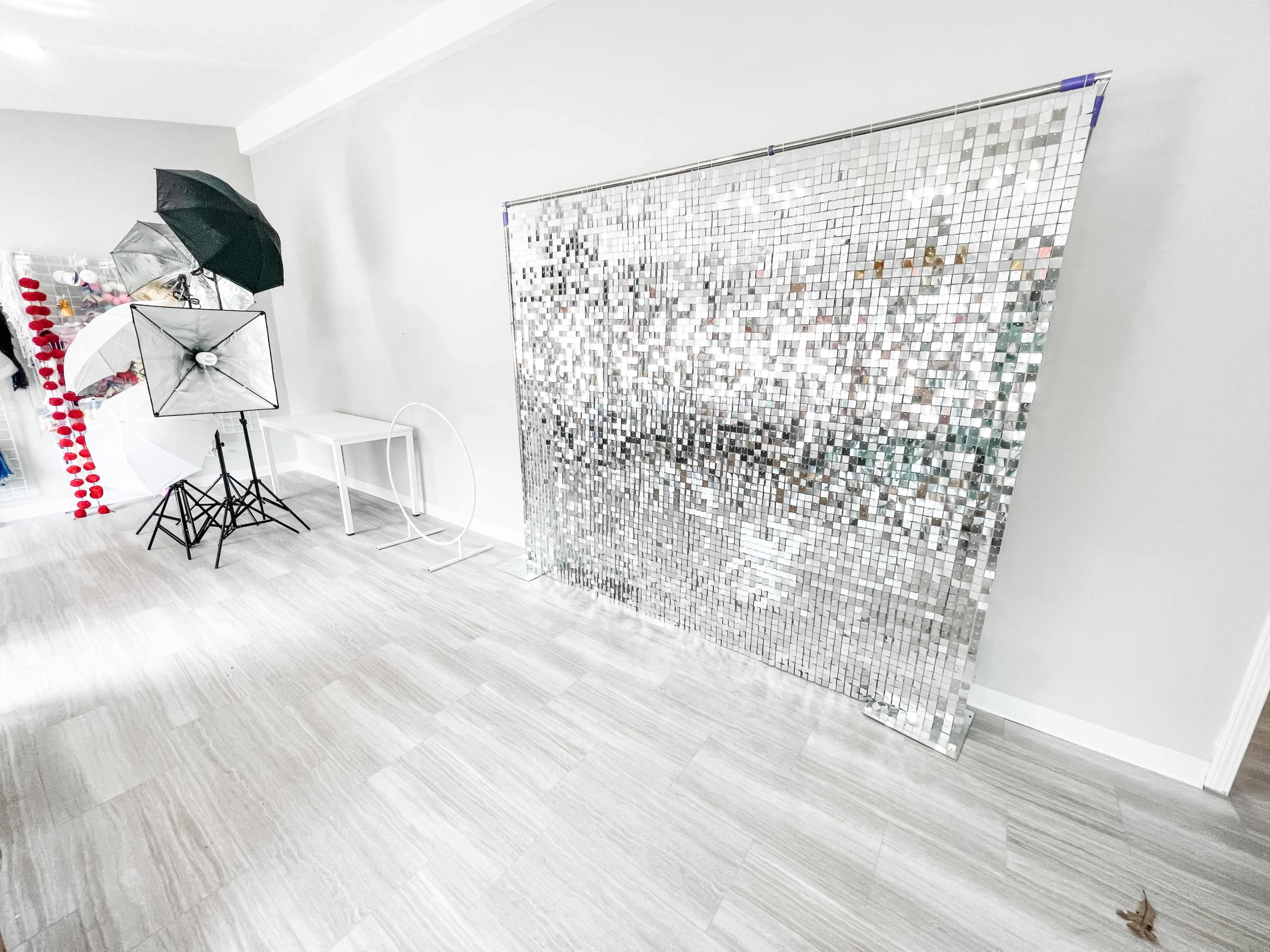A photography setup with a mirrored backdrop, lighting equipment, and a simple table in a well-lit room.