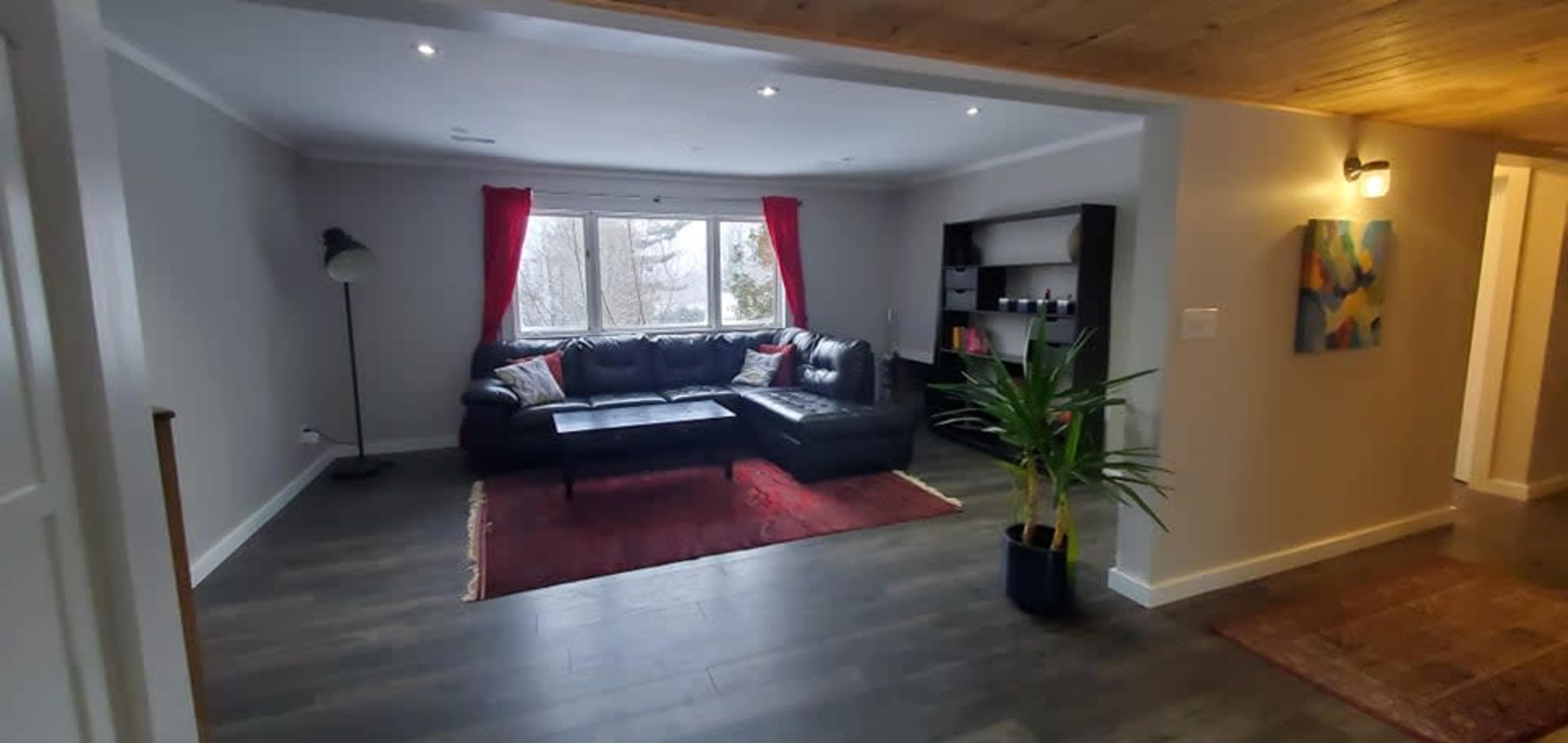 The living room features a black sectional couch, a coffee table on a red rug, and large windows with red curtains overlooking a snowy landscape.