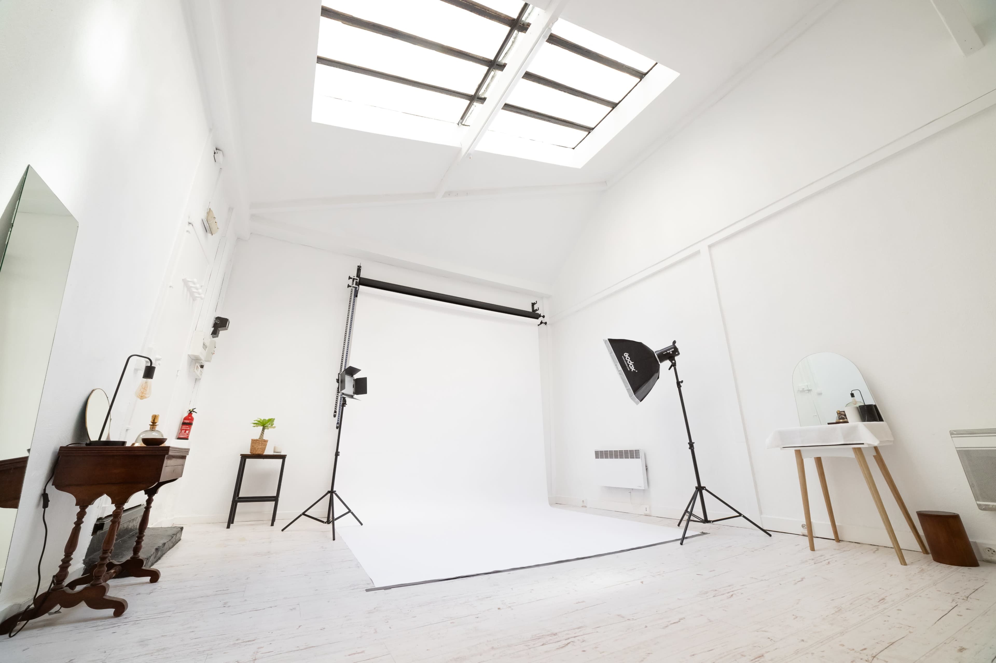 A bright photography studio features a white backdrop, lighting equipment, and minimal furnishings.