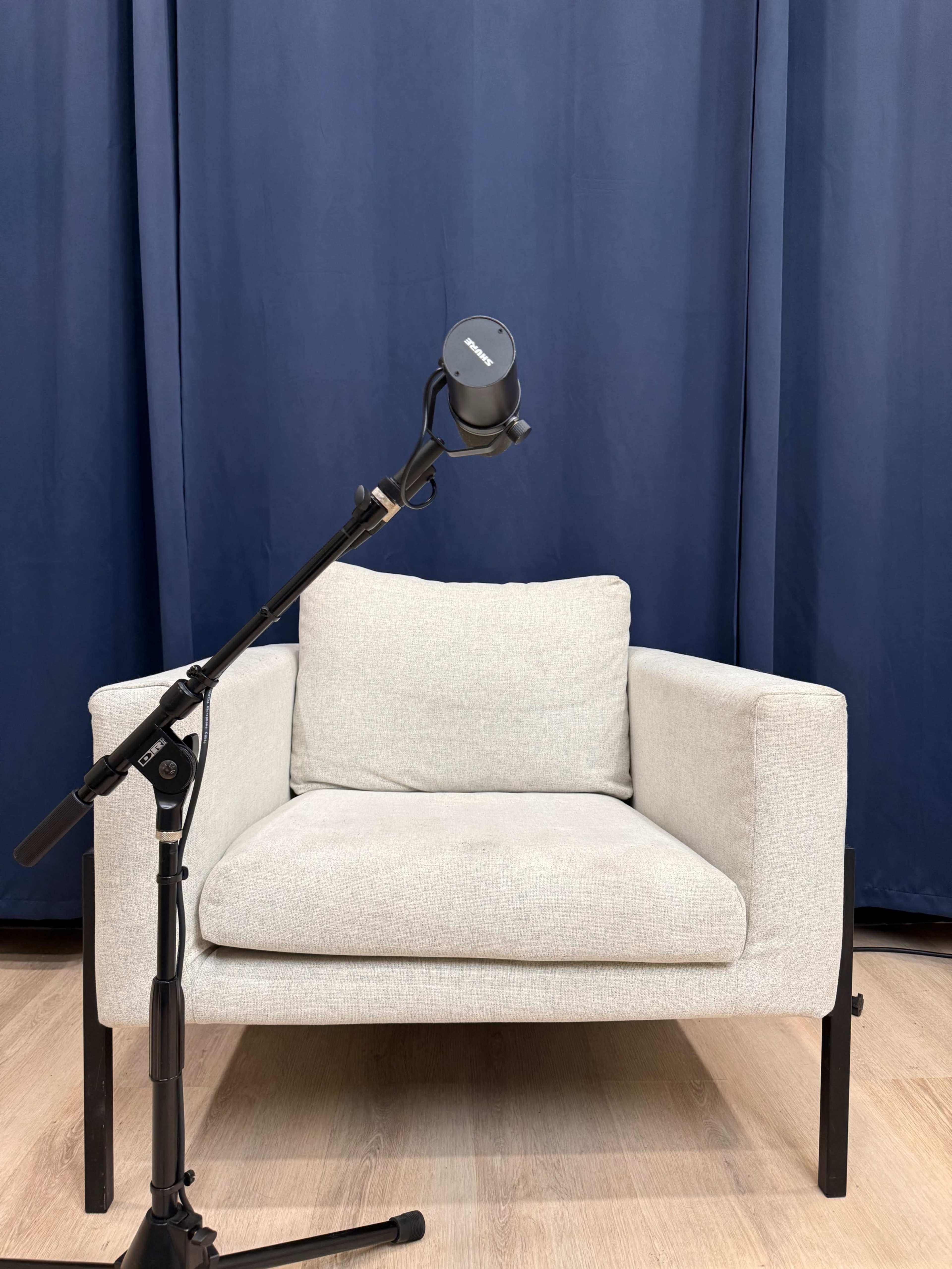 A gray armchair is positioned in front of a blue curtain, accompanied by a microphone mounted on a stand.