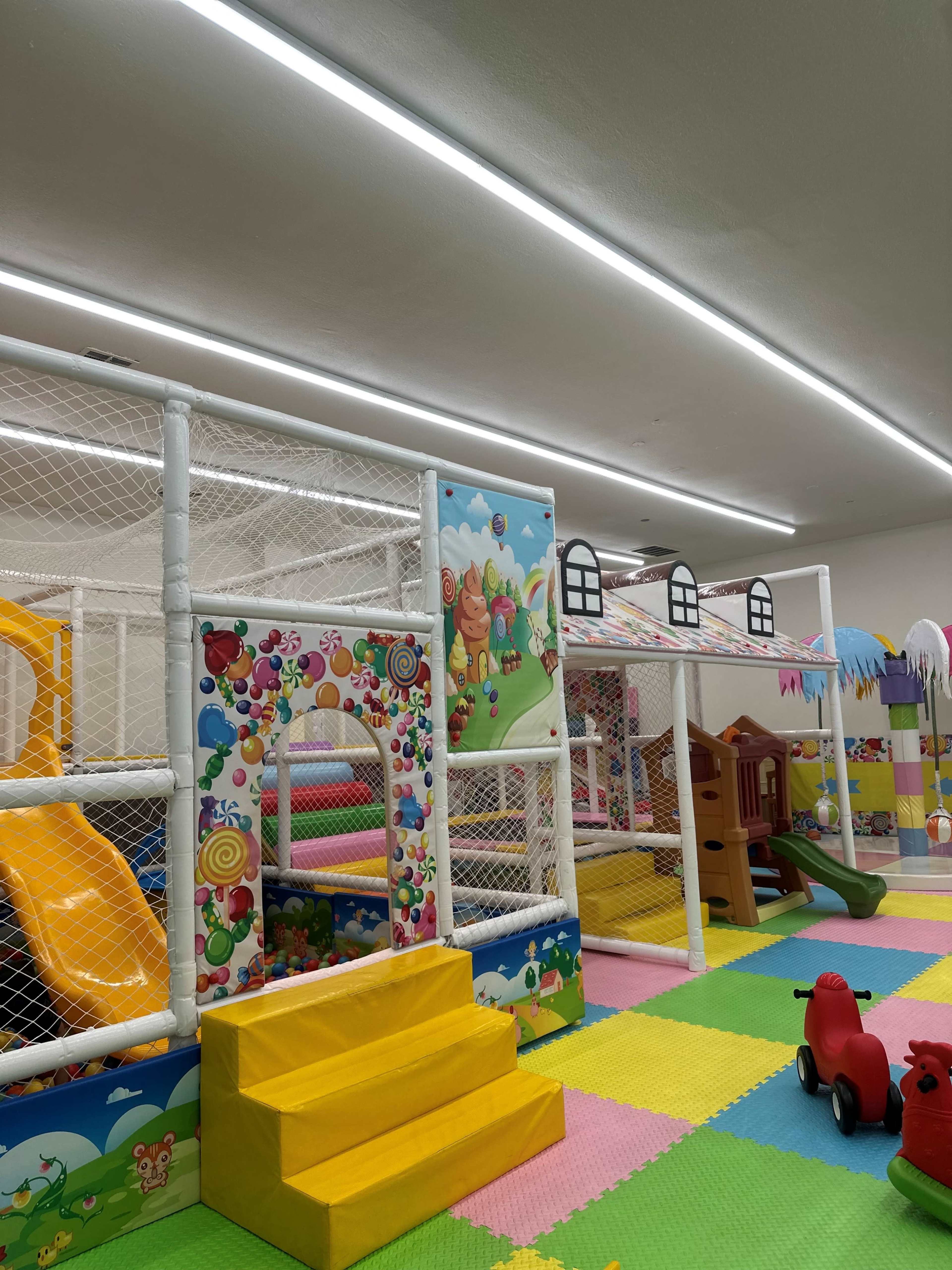 A colorful indoor play area with a plastic play structure, slides, and various toys on a patterned rubber floor.