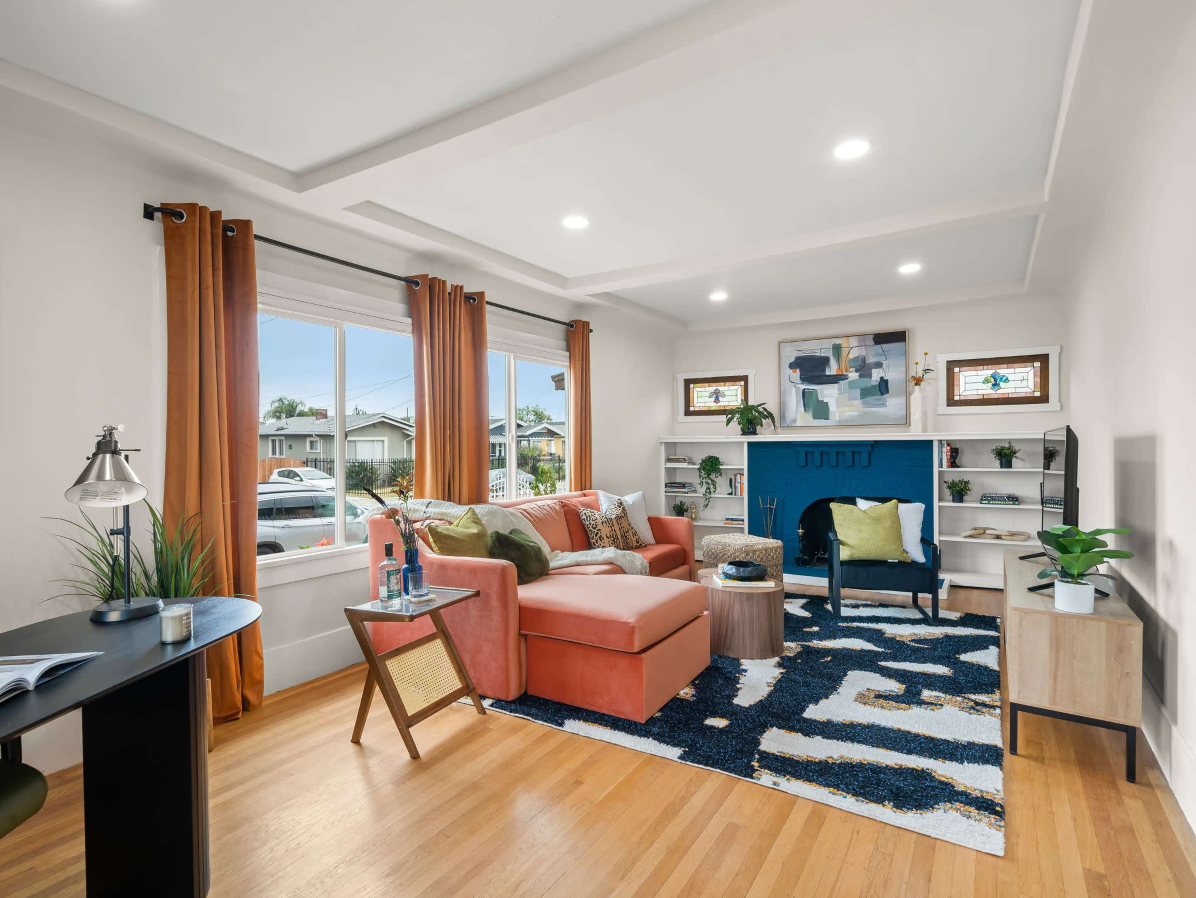 The living room features a coral sofa, blue accent wall, and large windows with orange curtains, along with a wooden coffee table and patterned rug.