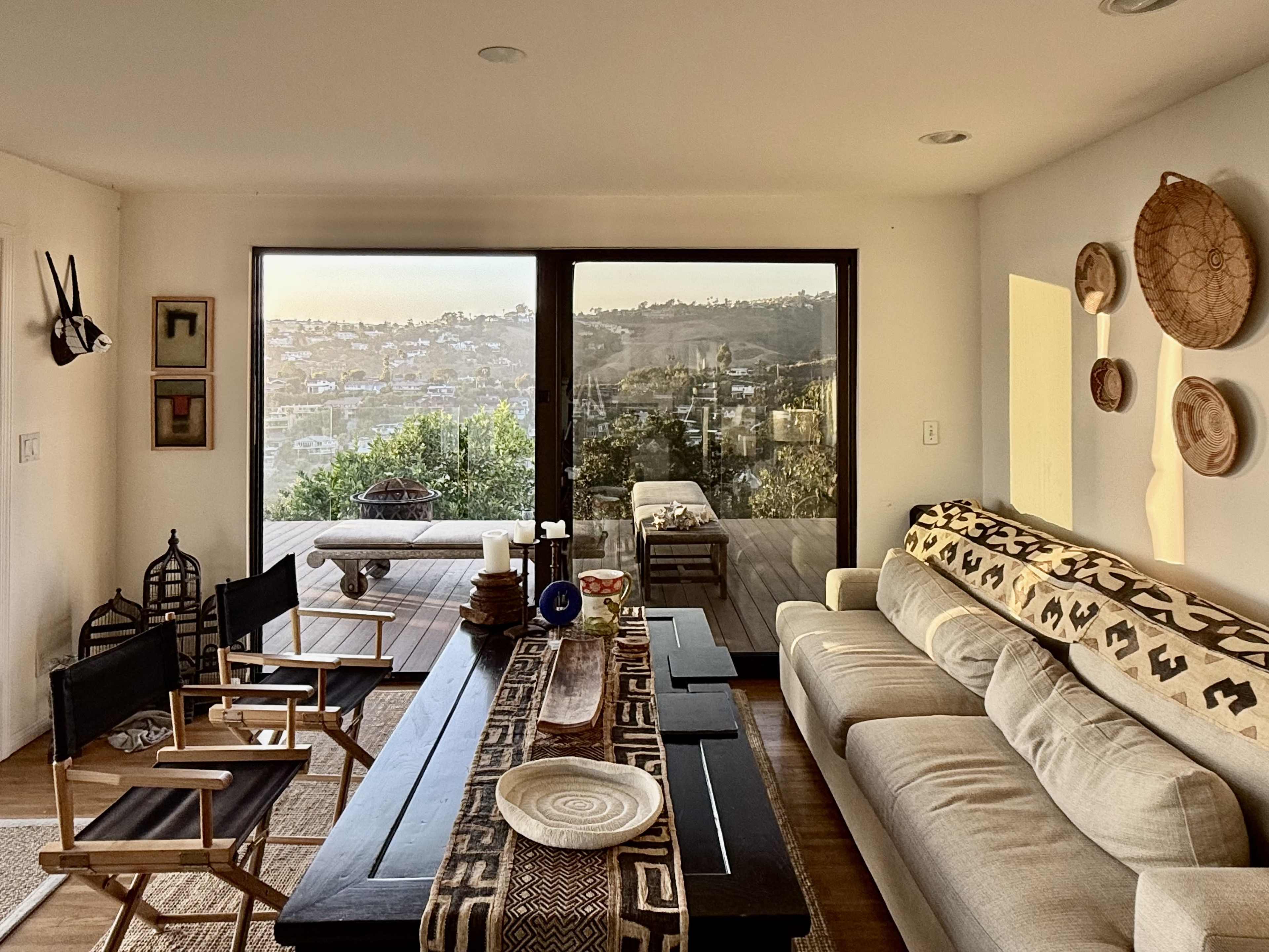 A modern living room features a neutral sofa, wooden coffee table, and a large window overlooking a scenic view.
