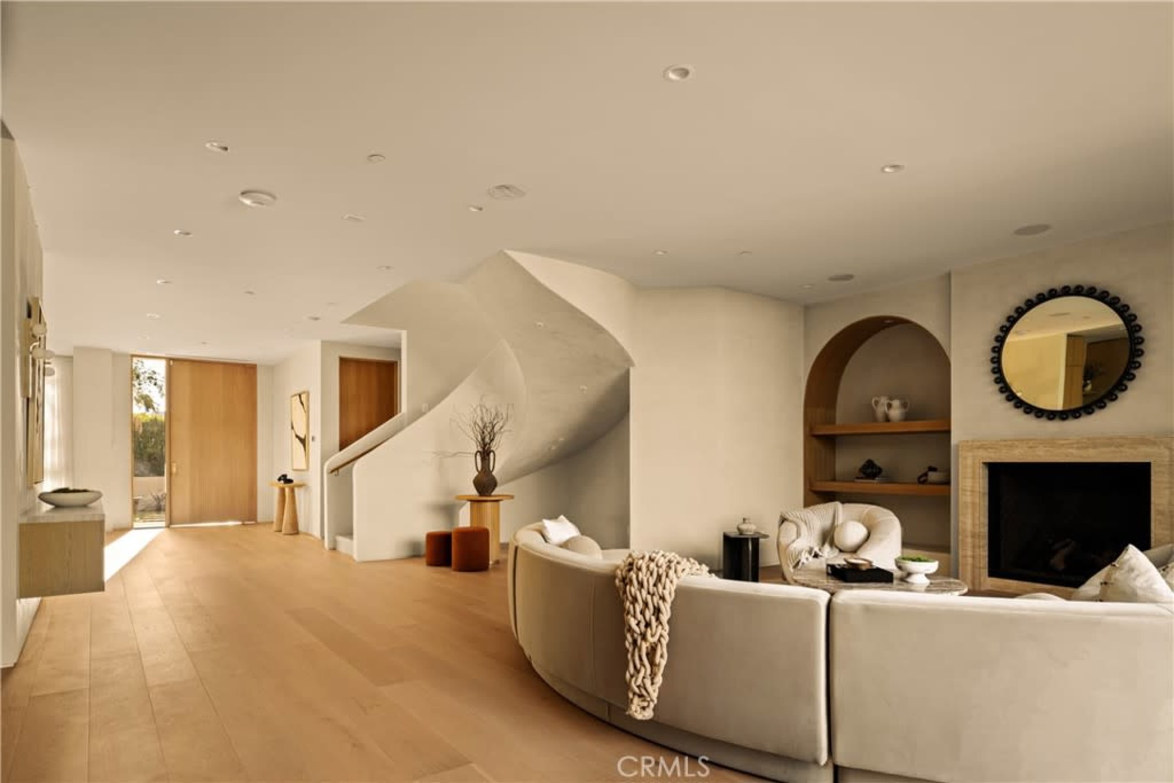 The image shows a modern interior living space featuring a curved sofa, minimalist decor, and a staircase leading to another area of the home.