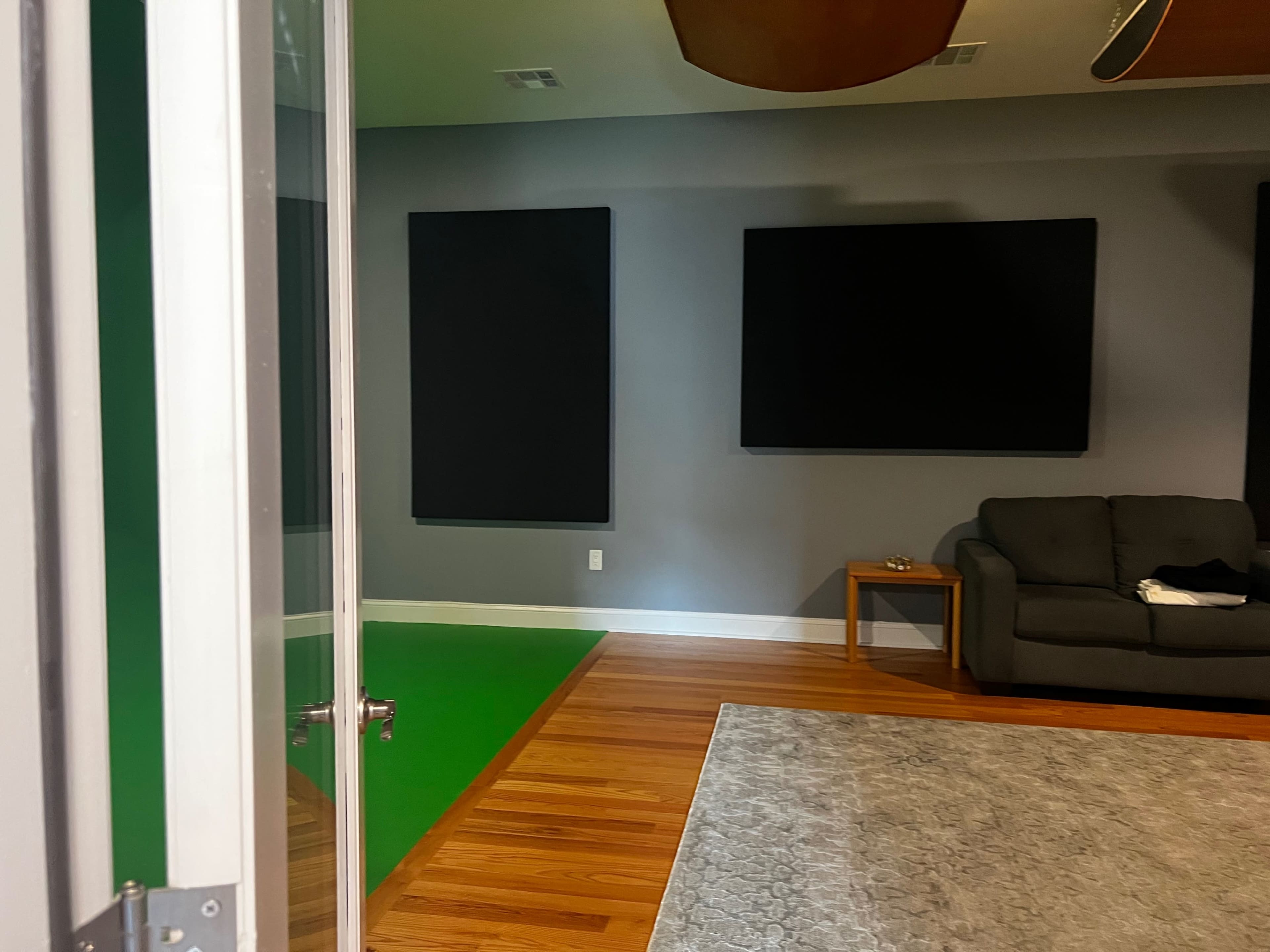 A room with green flooring, two large black panels on the walls, a gray wall, a couch, and a side table.