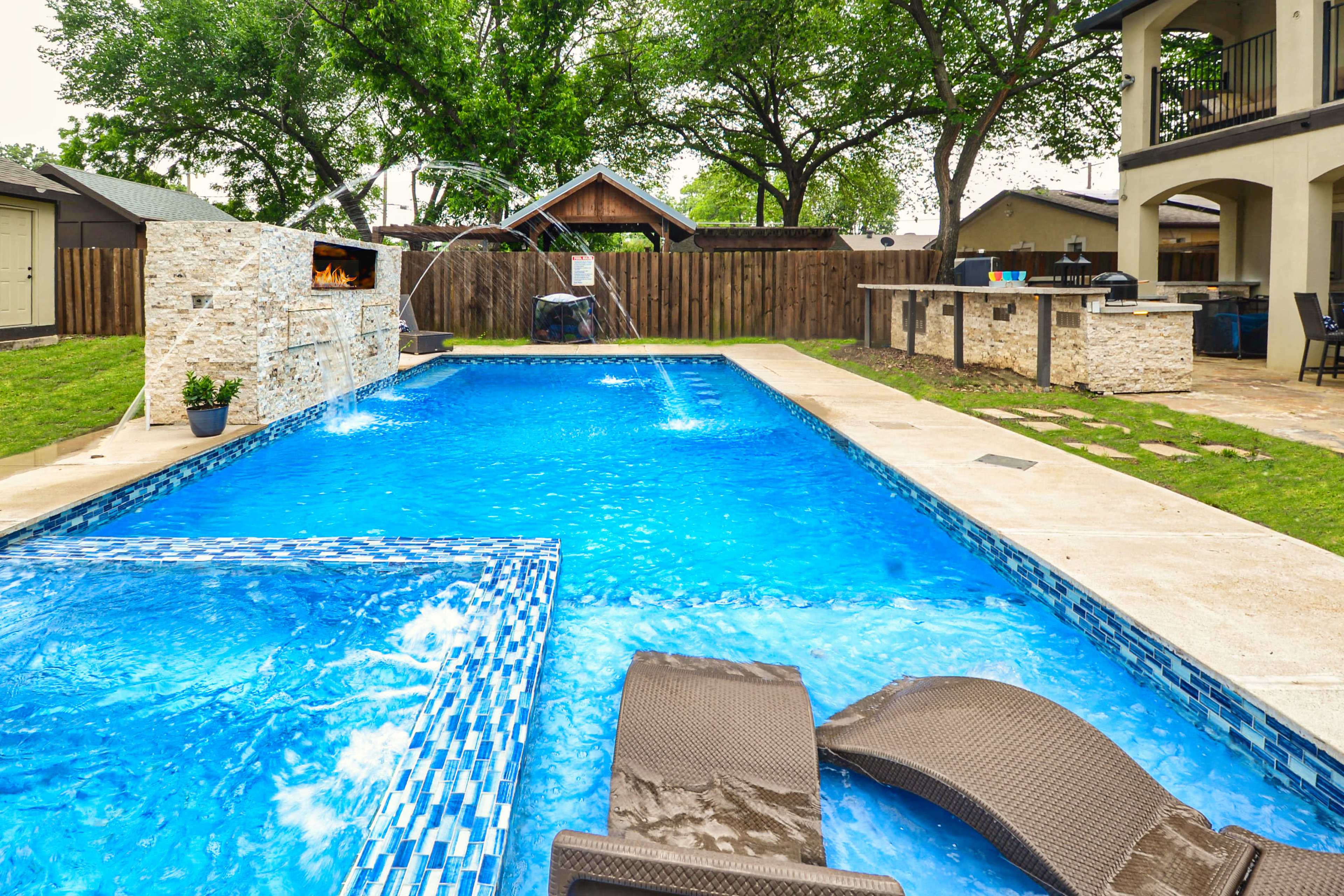 The image shows a backyard swimming pool with a spa area, surrounded by trees and a barbecue station.