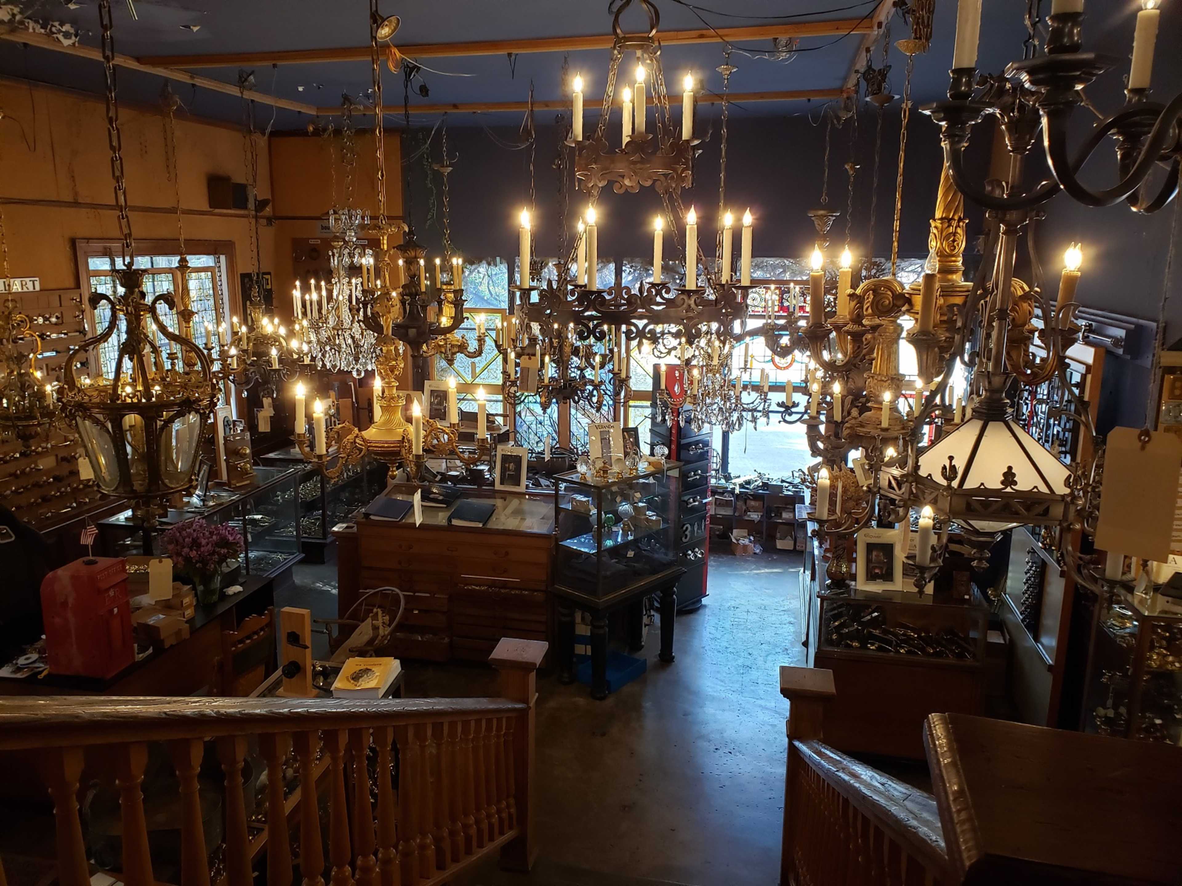 The image shows a well-lit antique shop filled with various chandeliers and display cases arranged in a spacious interior.