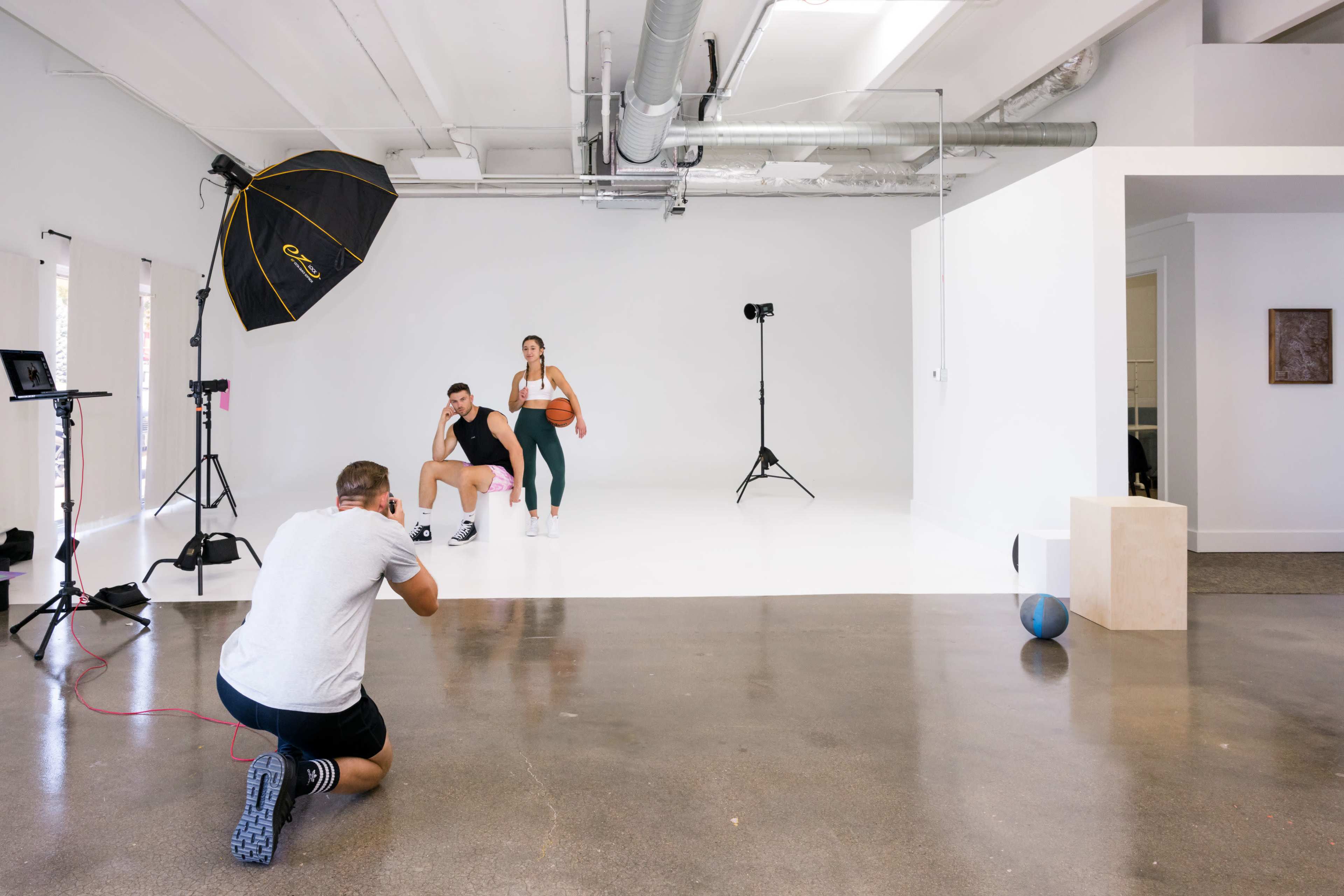 A photographer captures a shot of a woman holding a basketball and a man sitting next to her in a studio with a plain white backdrop.
