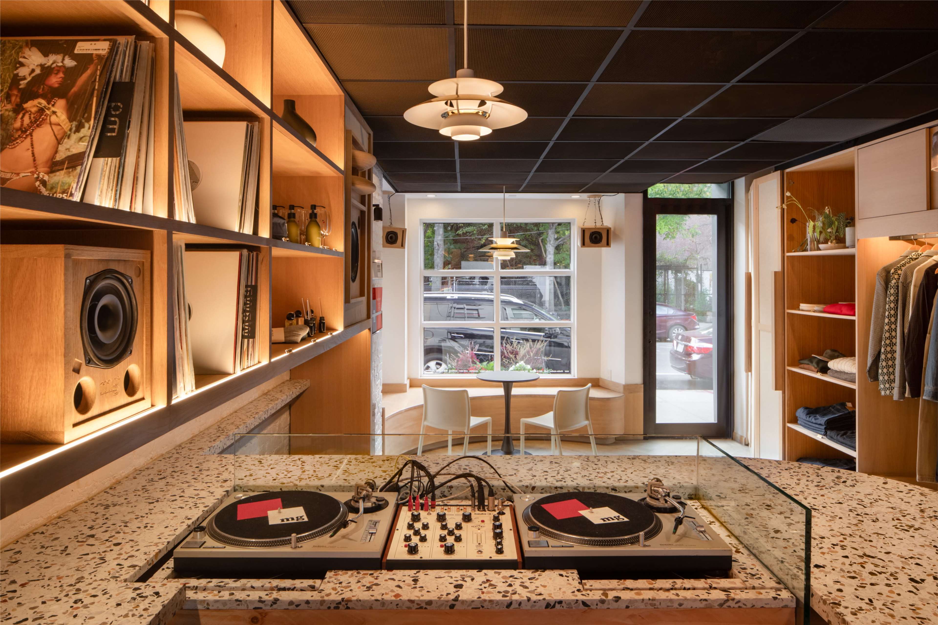 The image shows a stylish shop interior featuring a DJ turntable setup in the foreground, with wooden shelving displaying records and clothing in the background.
