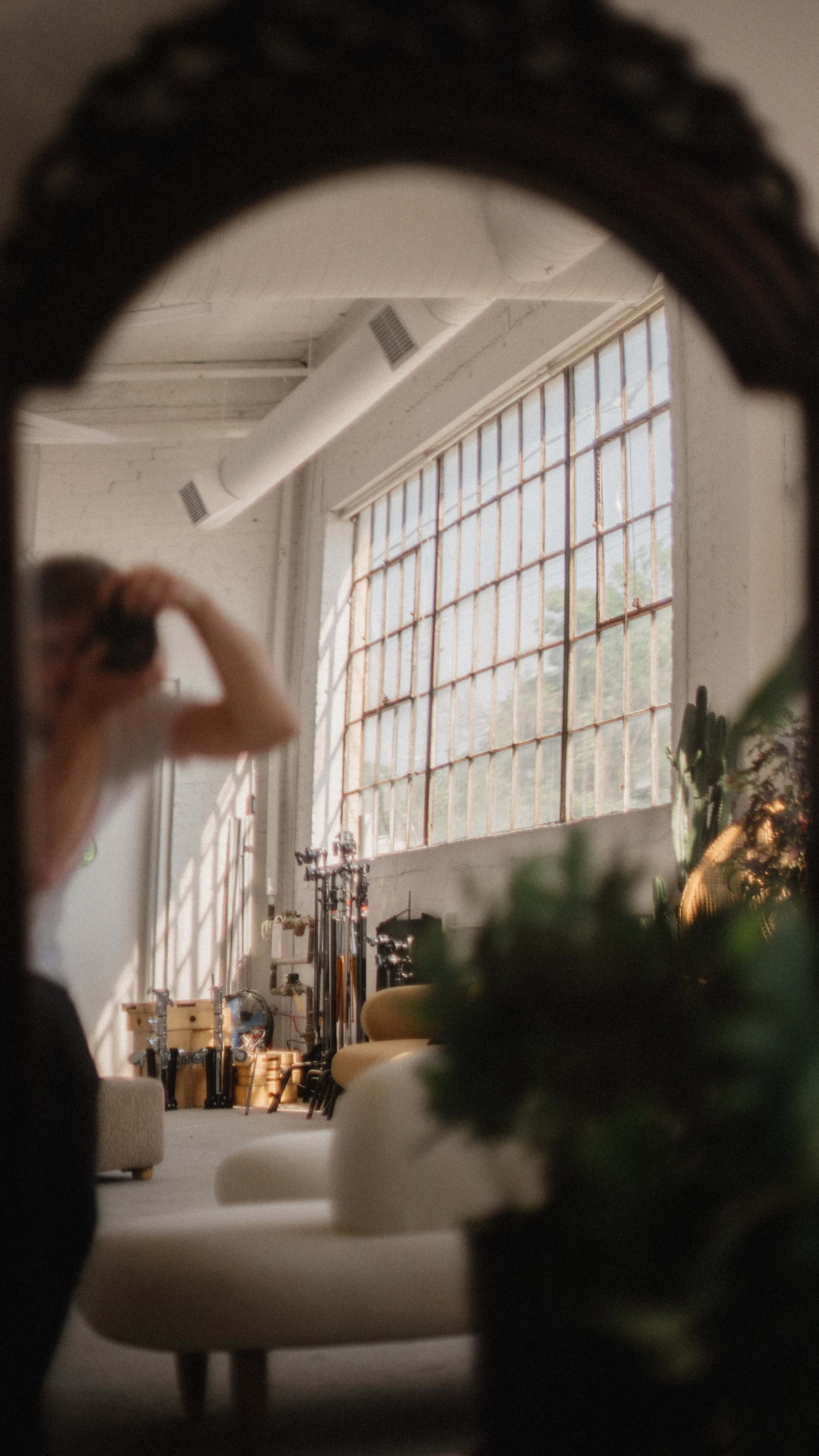 A person is reflected in a curved mirror, capturing the interior of a spacious room with large windows and various plants.