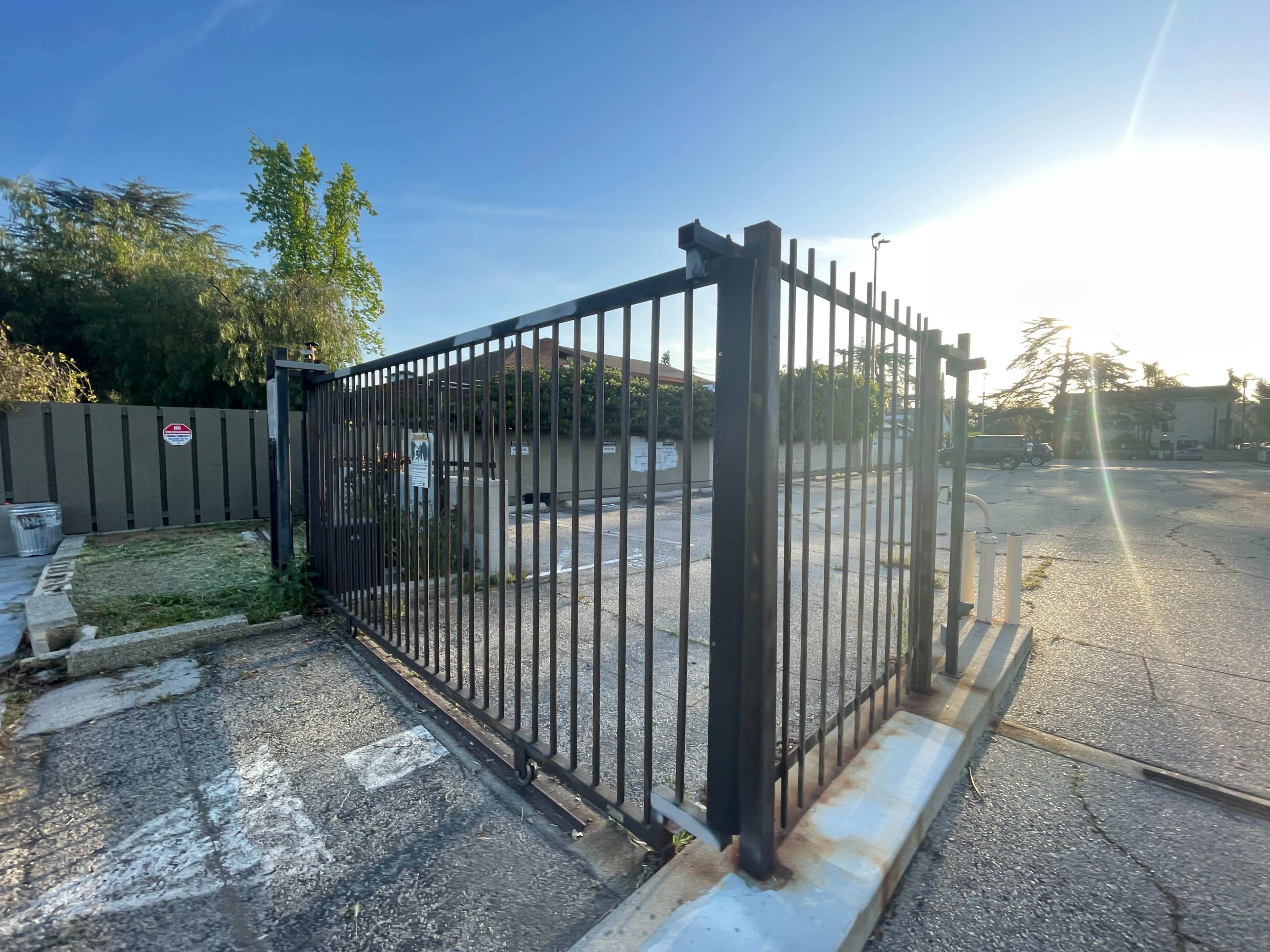 A metal gate stands open in an empty parking lot under a clear blue sky.