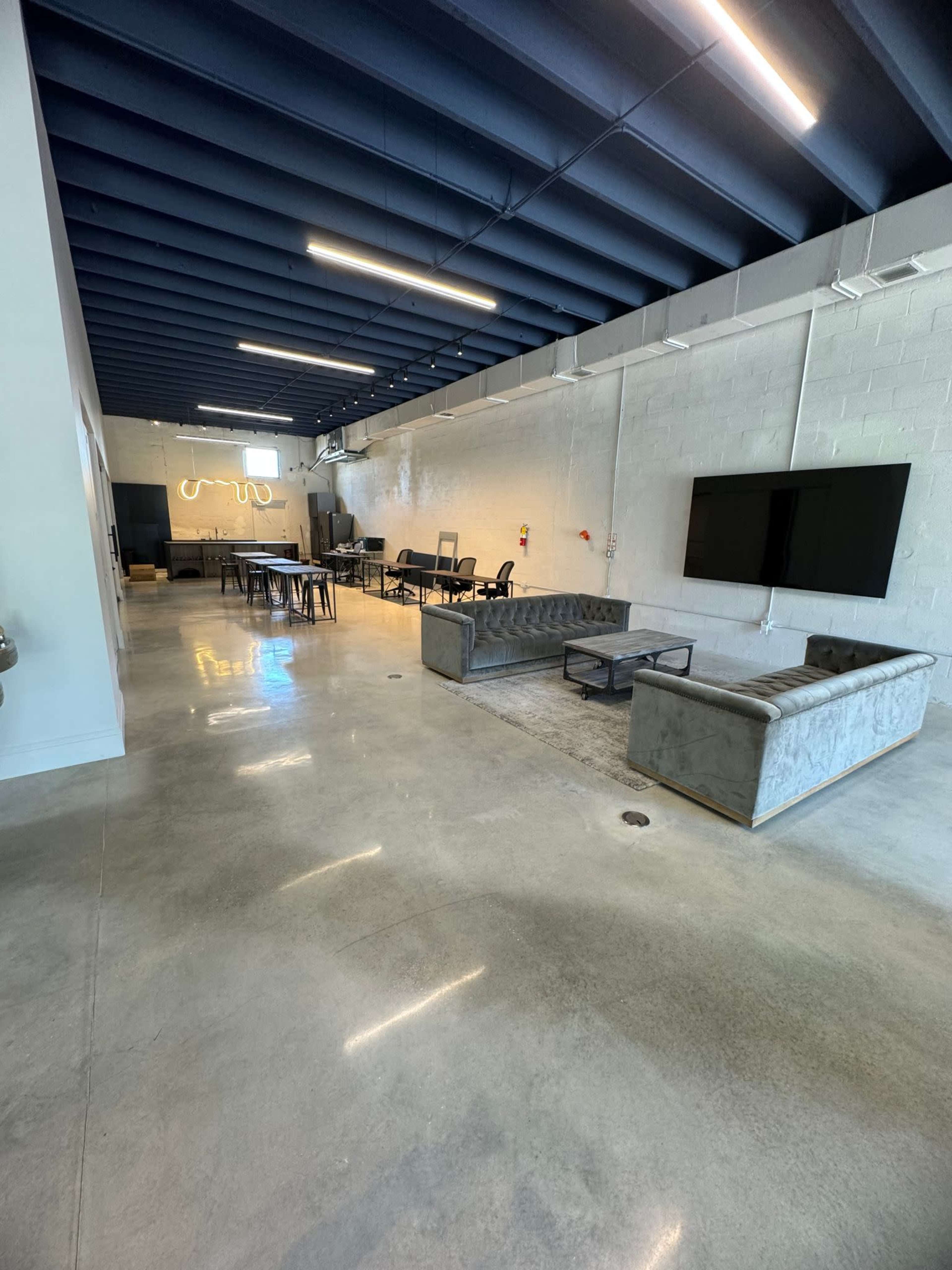 A spacious, modern interior with polished concrete flooring, a seating area with gray sofas, and a dining area featuring a long table and chairs.