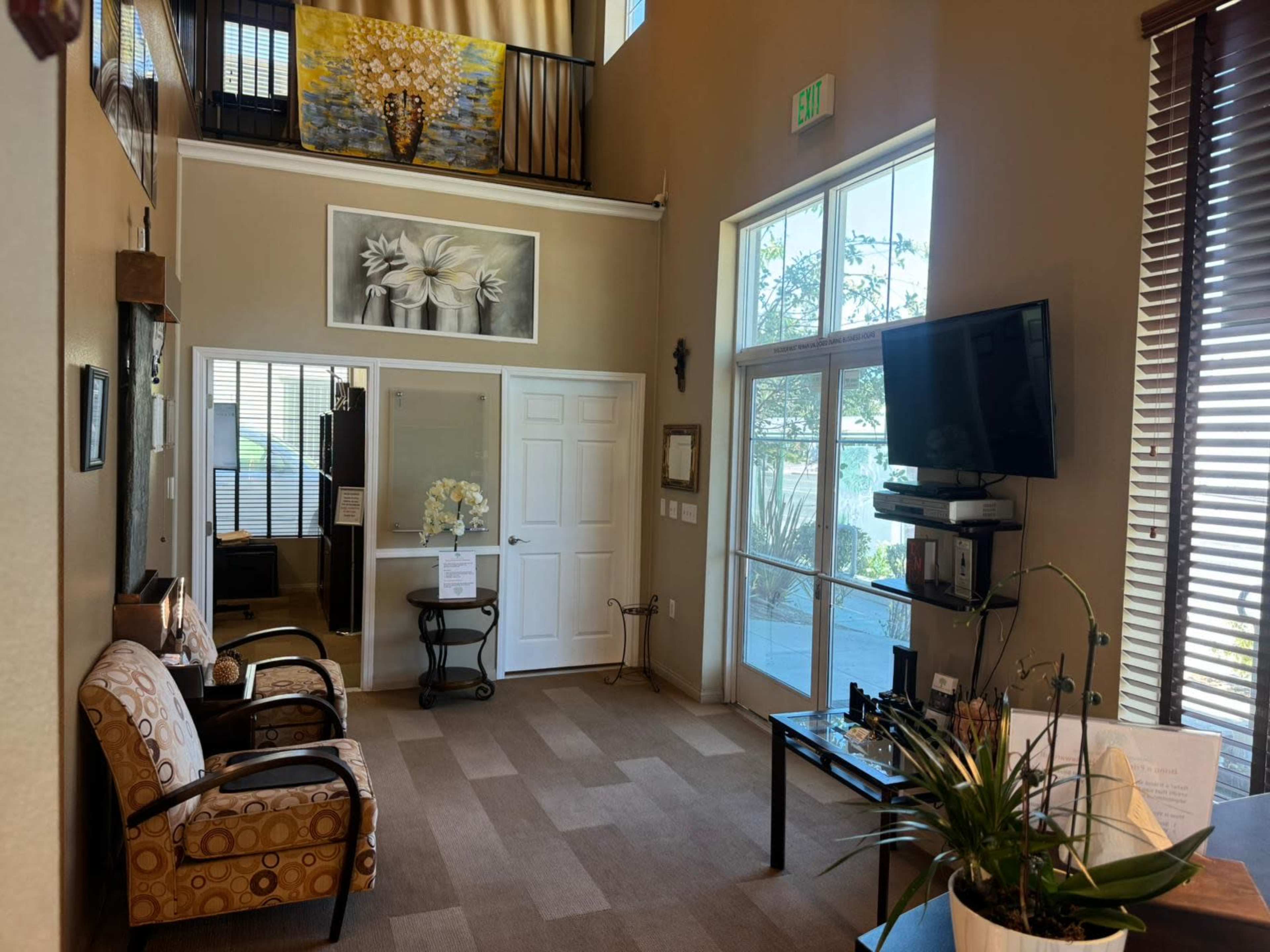 The image shows a well-lit reception area with a seating arrangement, a television, and a large window providing natural light.
