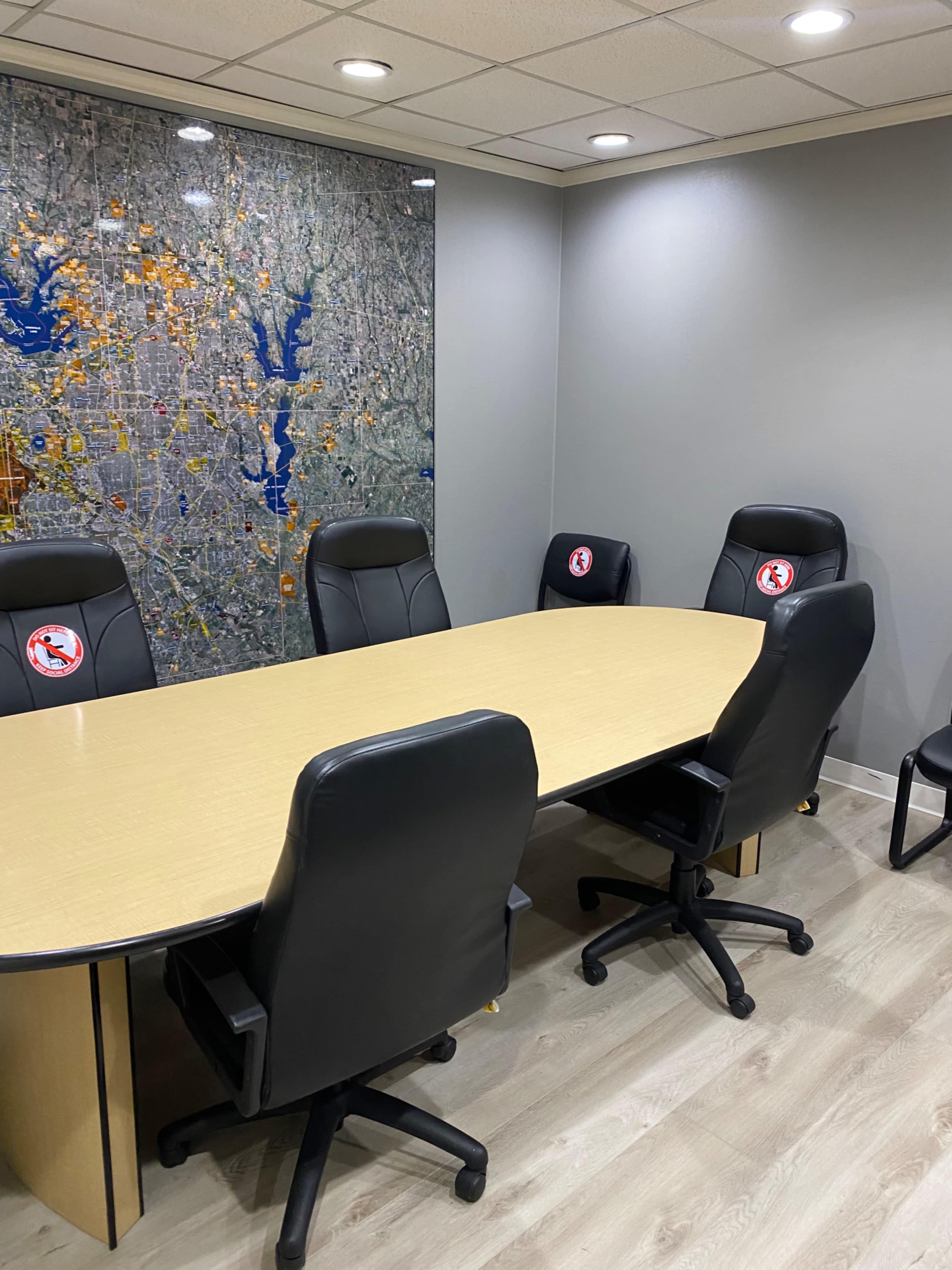 A conference room with a large oval table surrounded by six black leather chairs, and a wall featuring a map.
