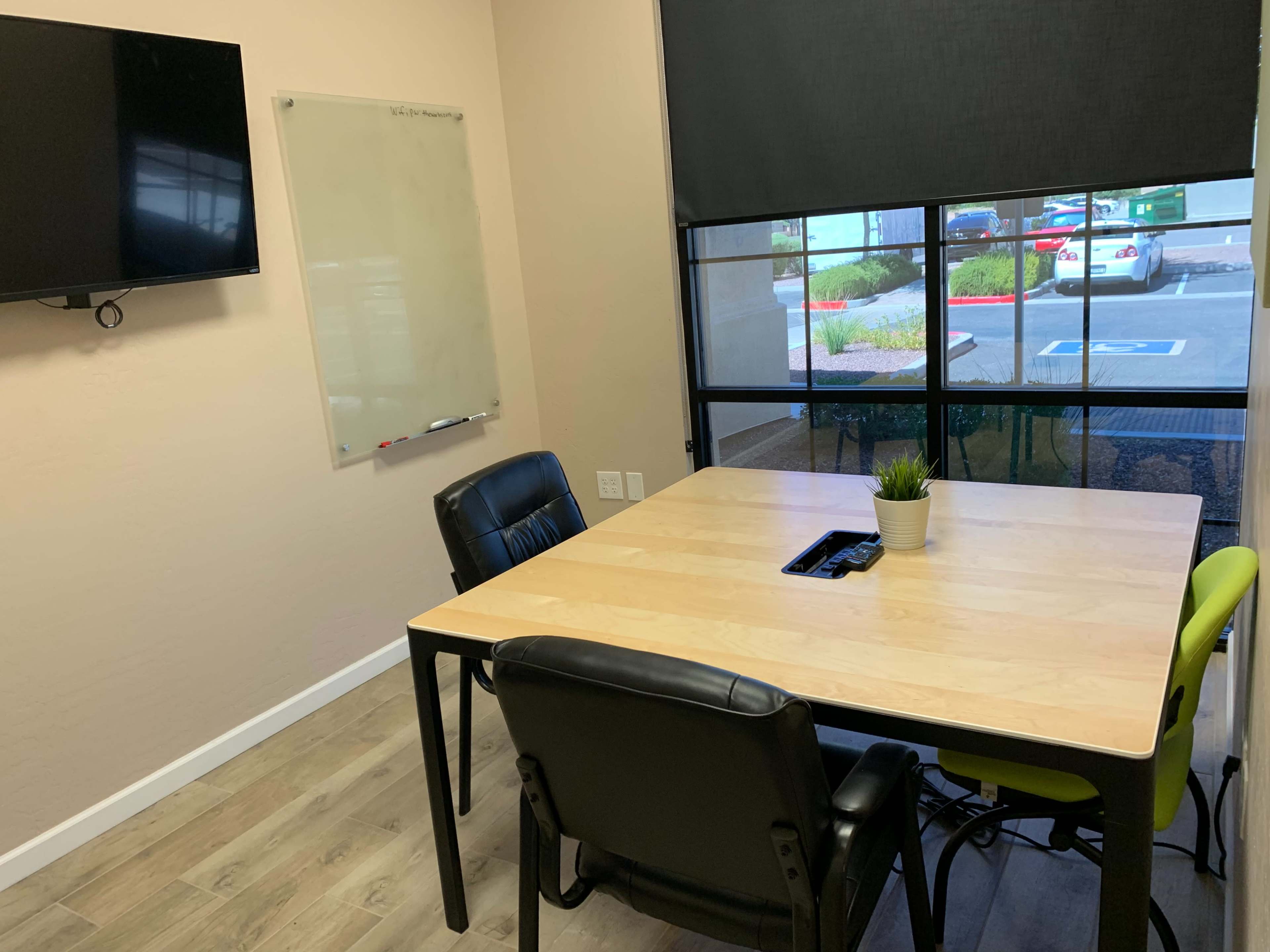 A meeting room features a wooden table with four chairs, a wall-mounted television, and a whiteboard.
