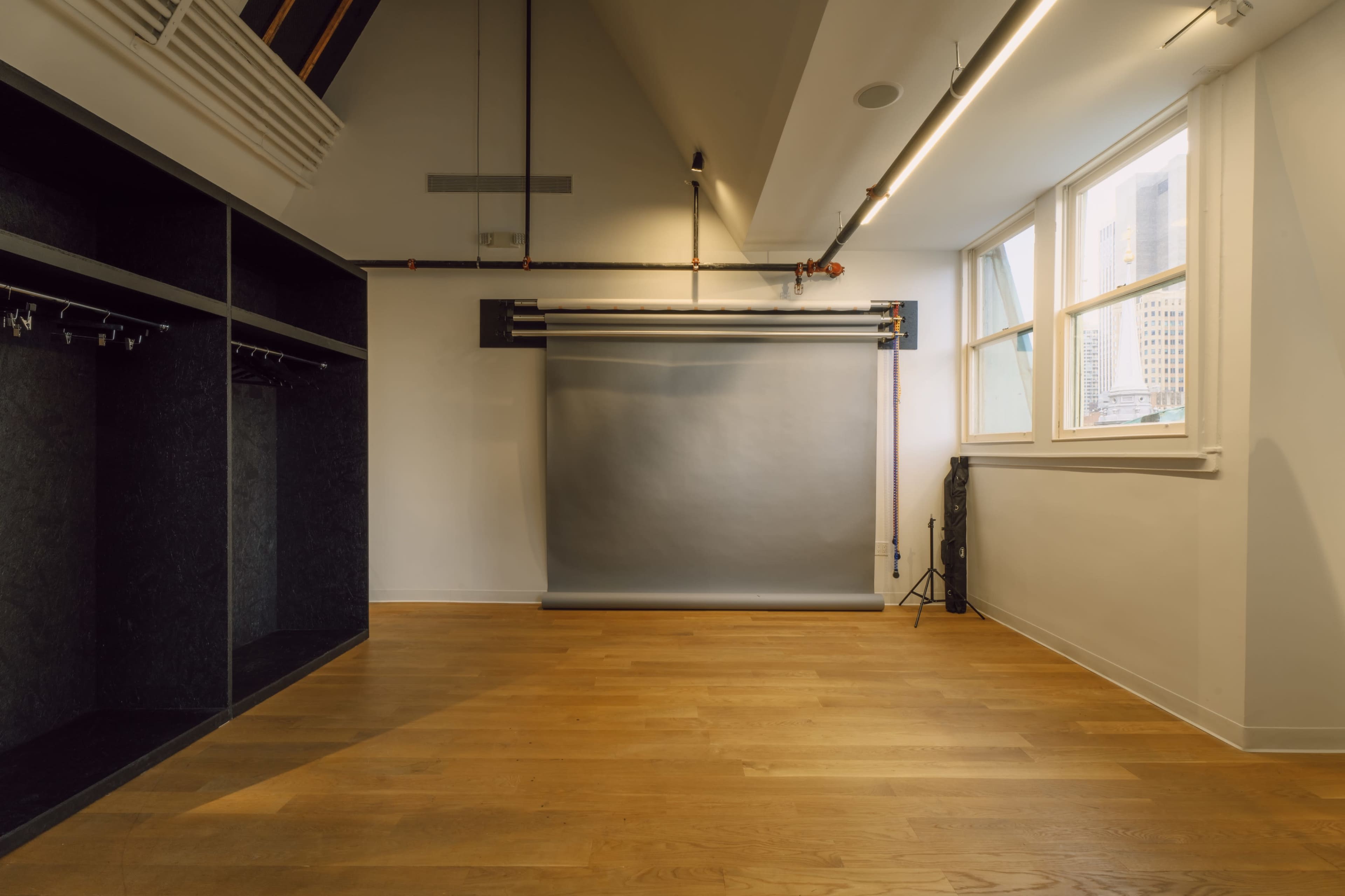The image shows an empty studio space with a wooden floor, a gray backdrop, and large windows letting in natural light.