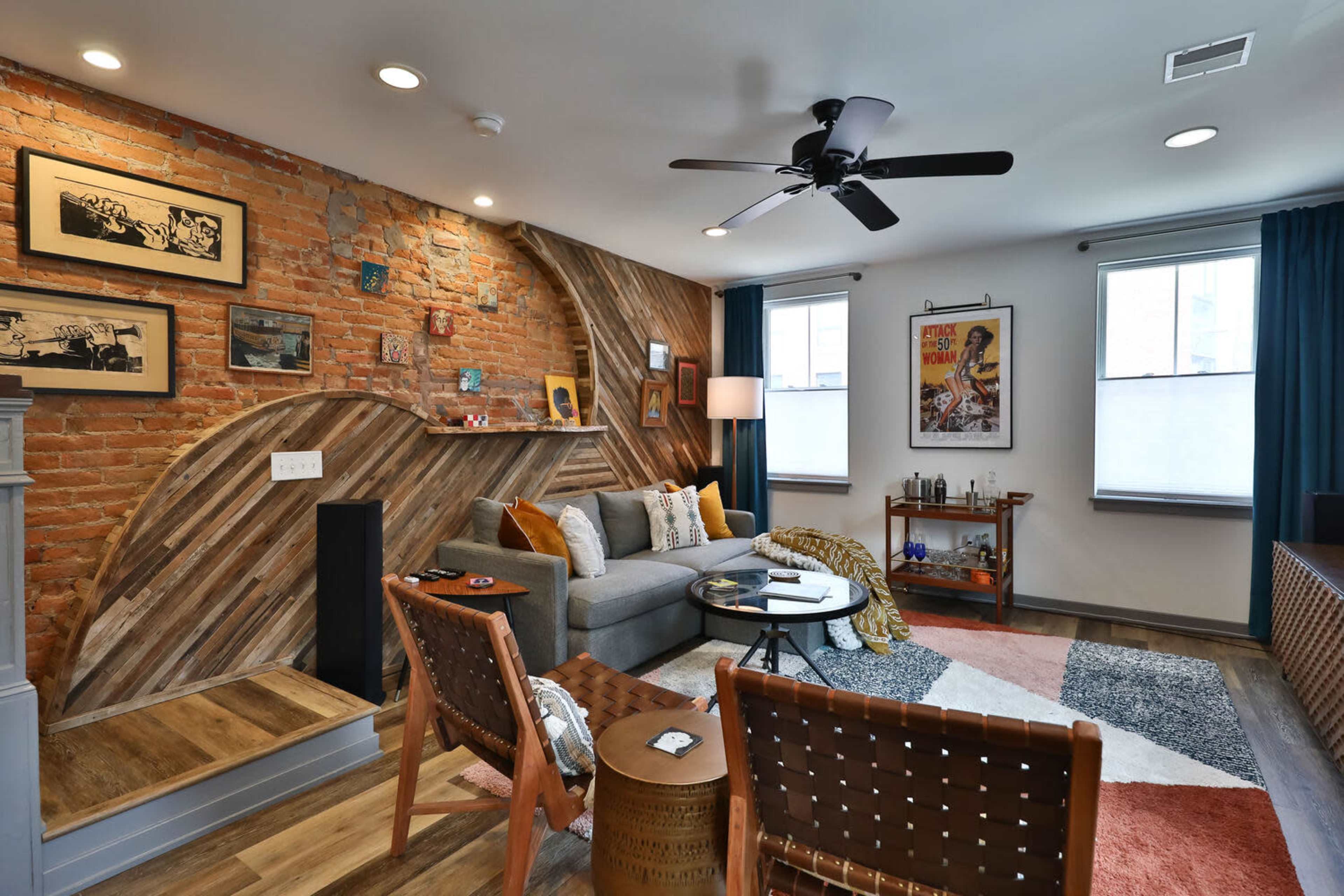 The living room features a brick wall, a grey sofa, and a mix of decorative furniture arranged around a geometric area rug.