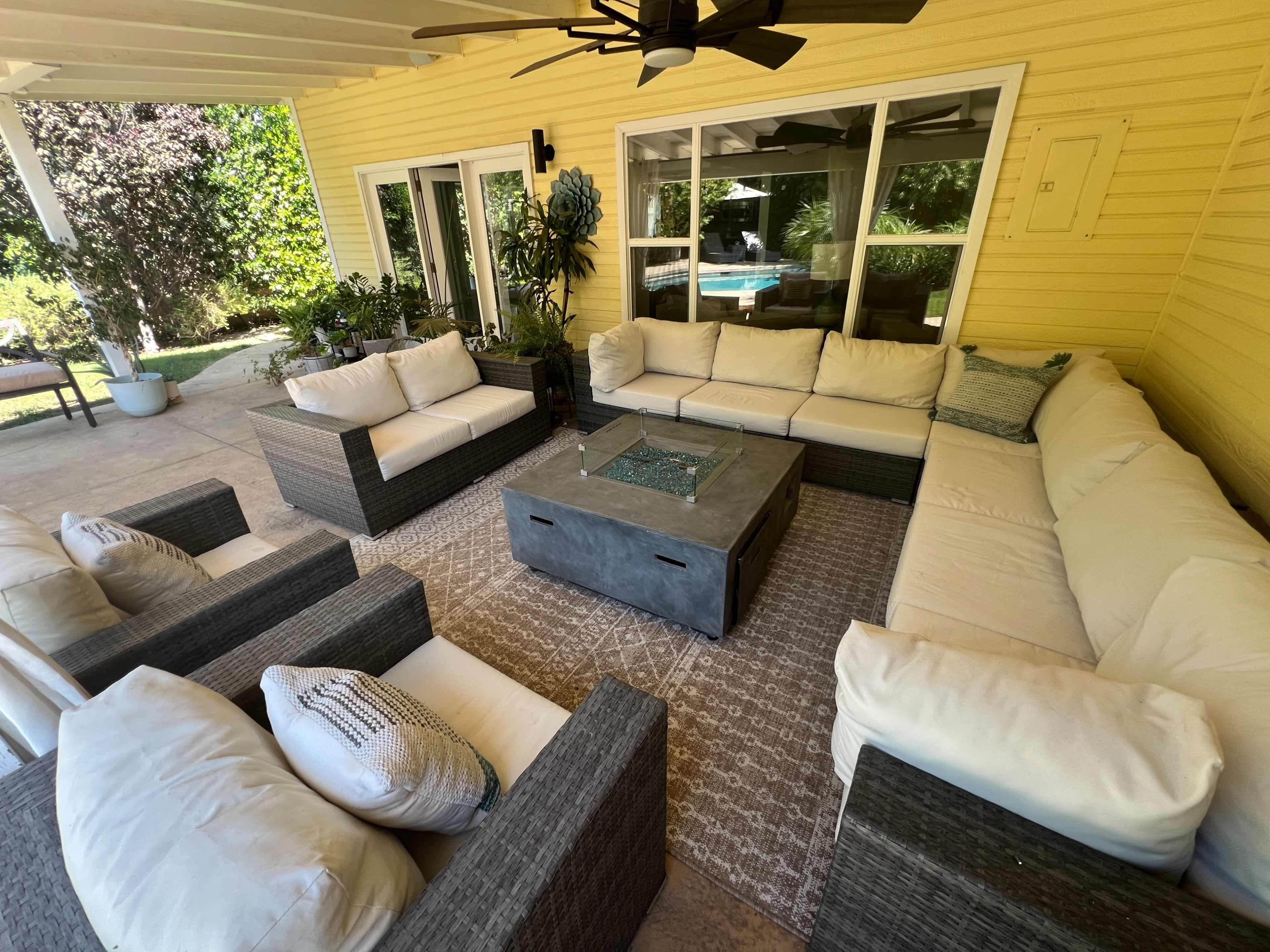 The image shows a comfortable outdoor lounge area with a sectional sofa and chairs arranged around a central coffee table on a tiled patio beside a backyard pool.
