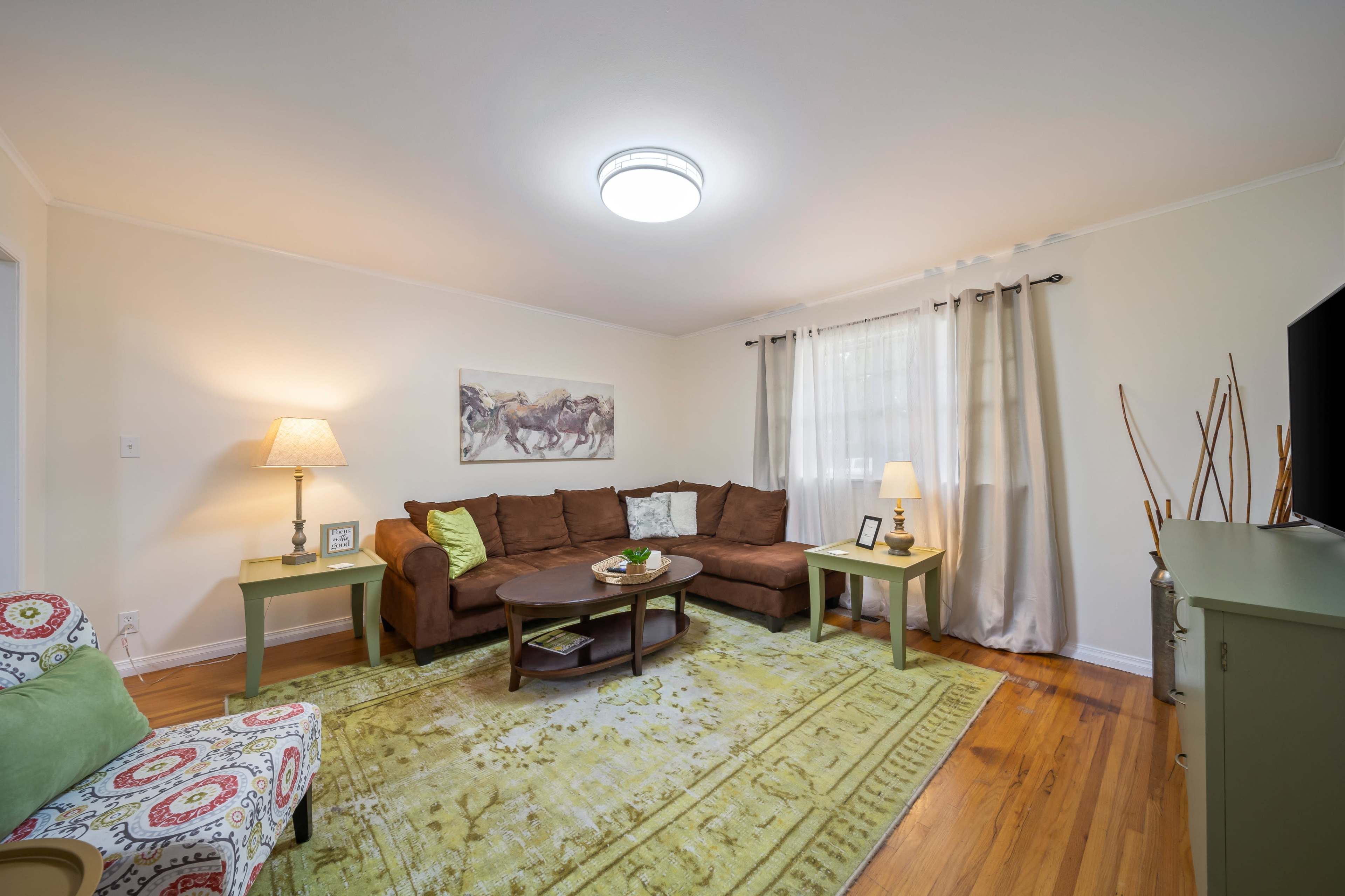 The living room features a brown sectional couch, a circular coffee table, and a green area rug, with a lamp and a television on a stand.