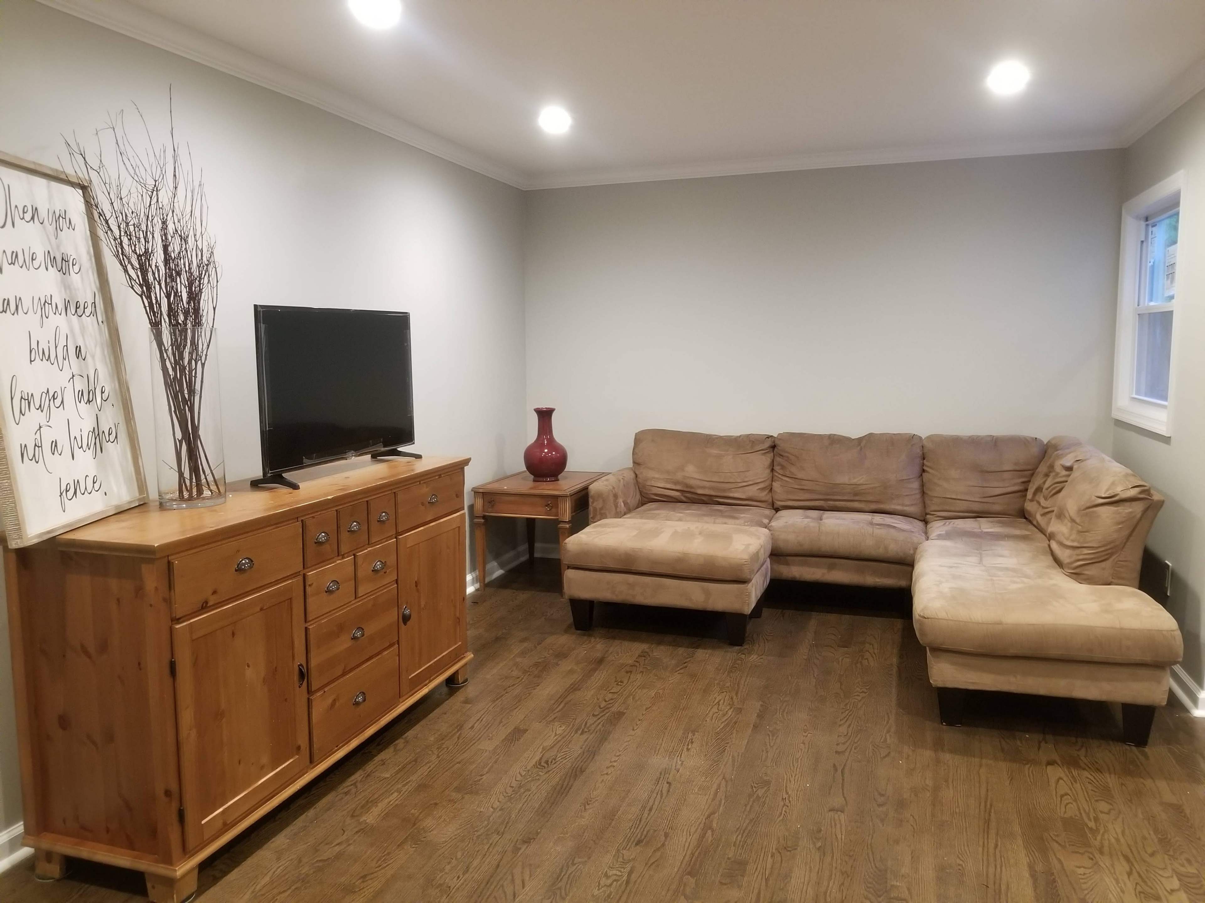 A living room features a brown sectional sofa, a wooden TV stand with a television, and a decorative vase on a side table.