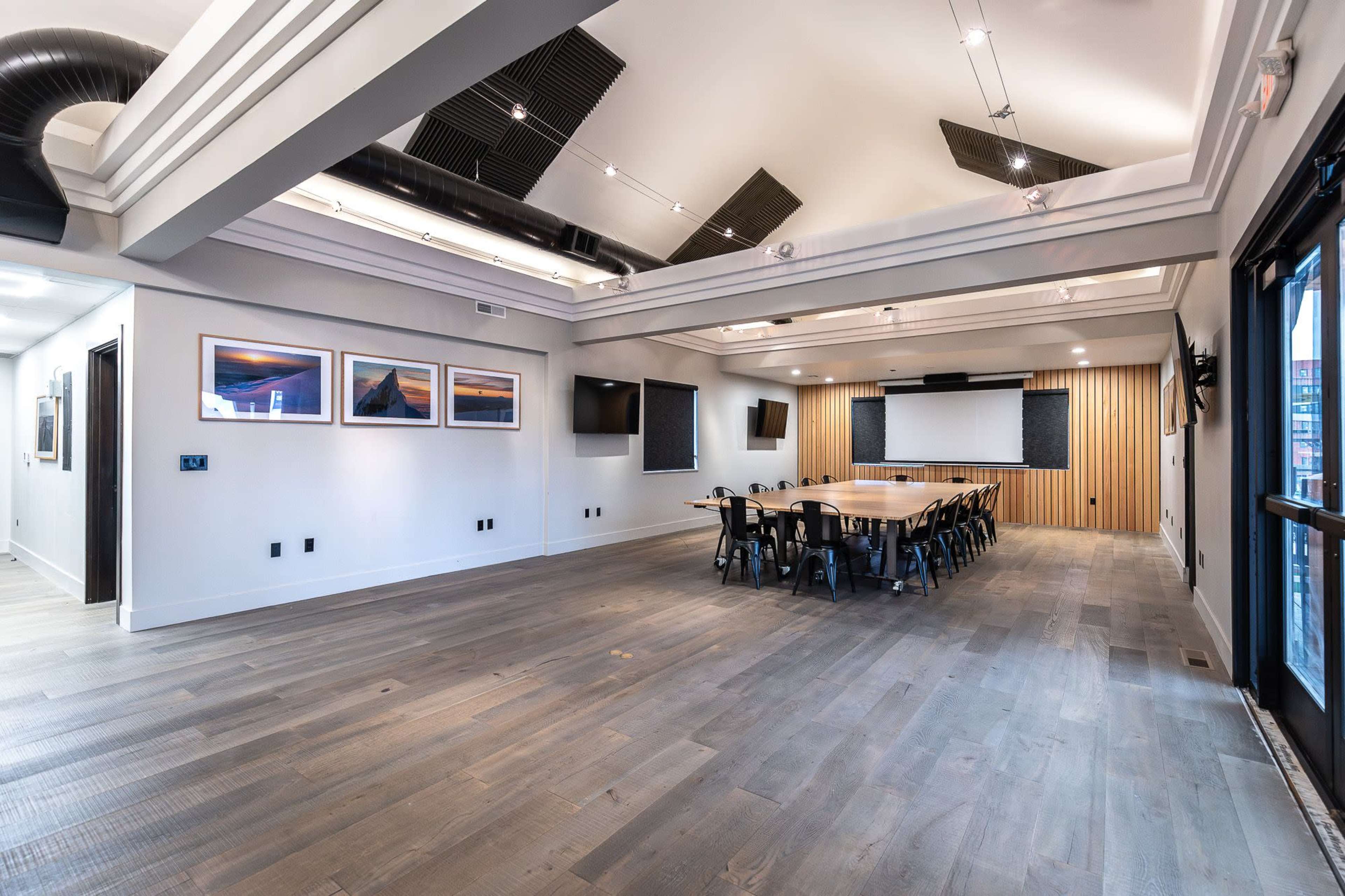 A modern conference room with a long table, several screens, and wooden paneling on the walls.