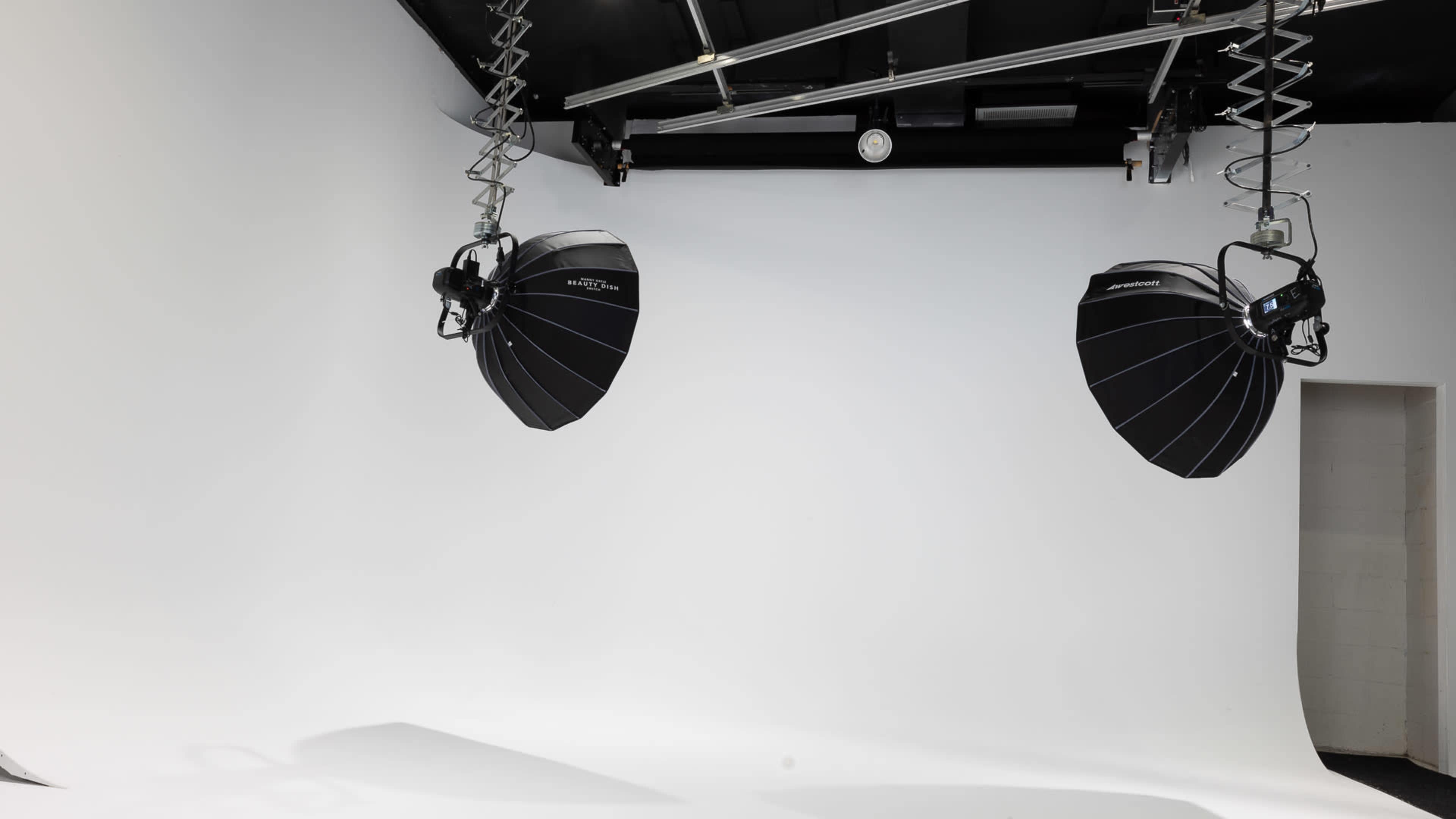 The image shows a photography studio with two large, suspended softbox lights and a seamless white backdrop.