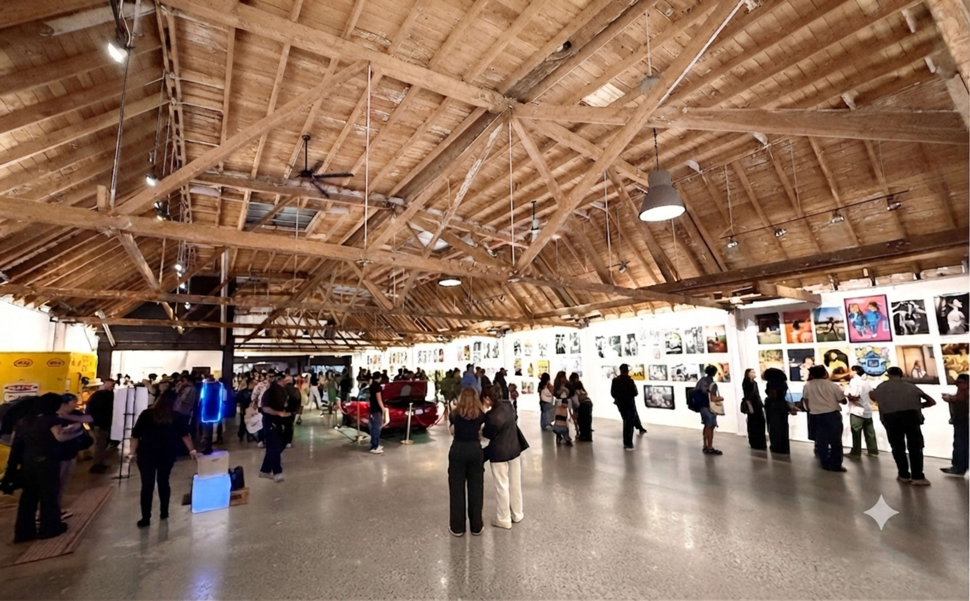 A crowd of people observes a gallery exhibition featuring a series of framed photographs displayed on the walls of a spacious, wooden-beamed venue.