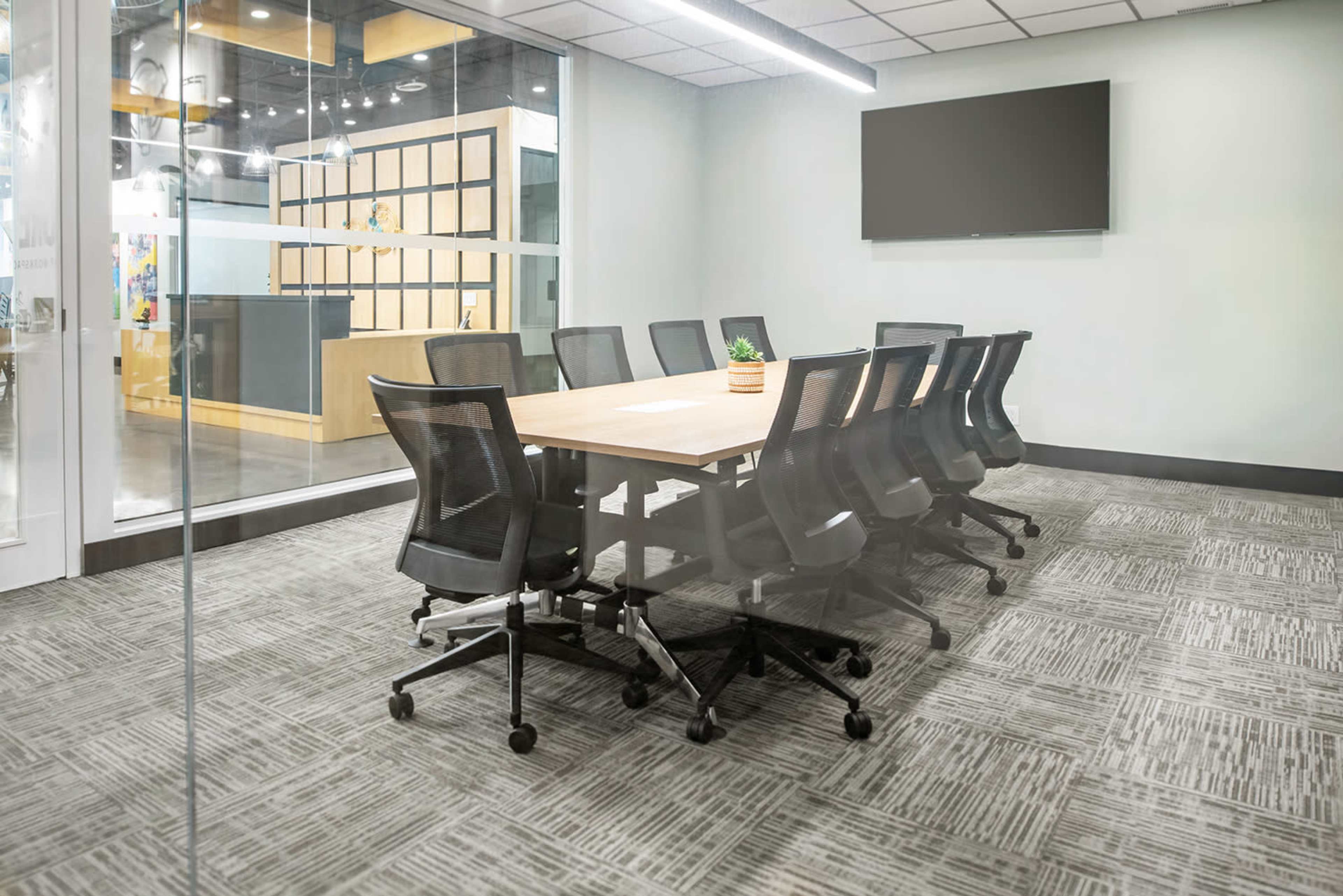 The image shows a modern conference room with a large table surrounded by eight chairs and a wall-mounted television.