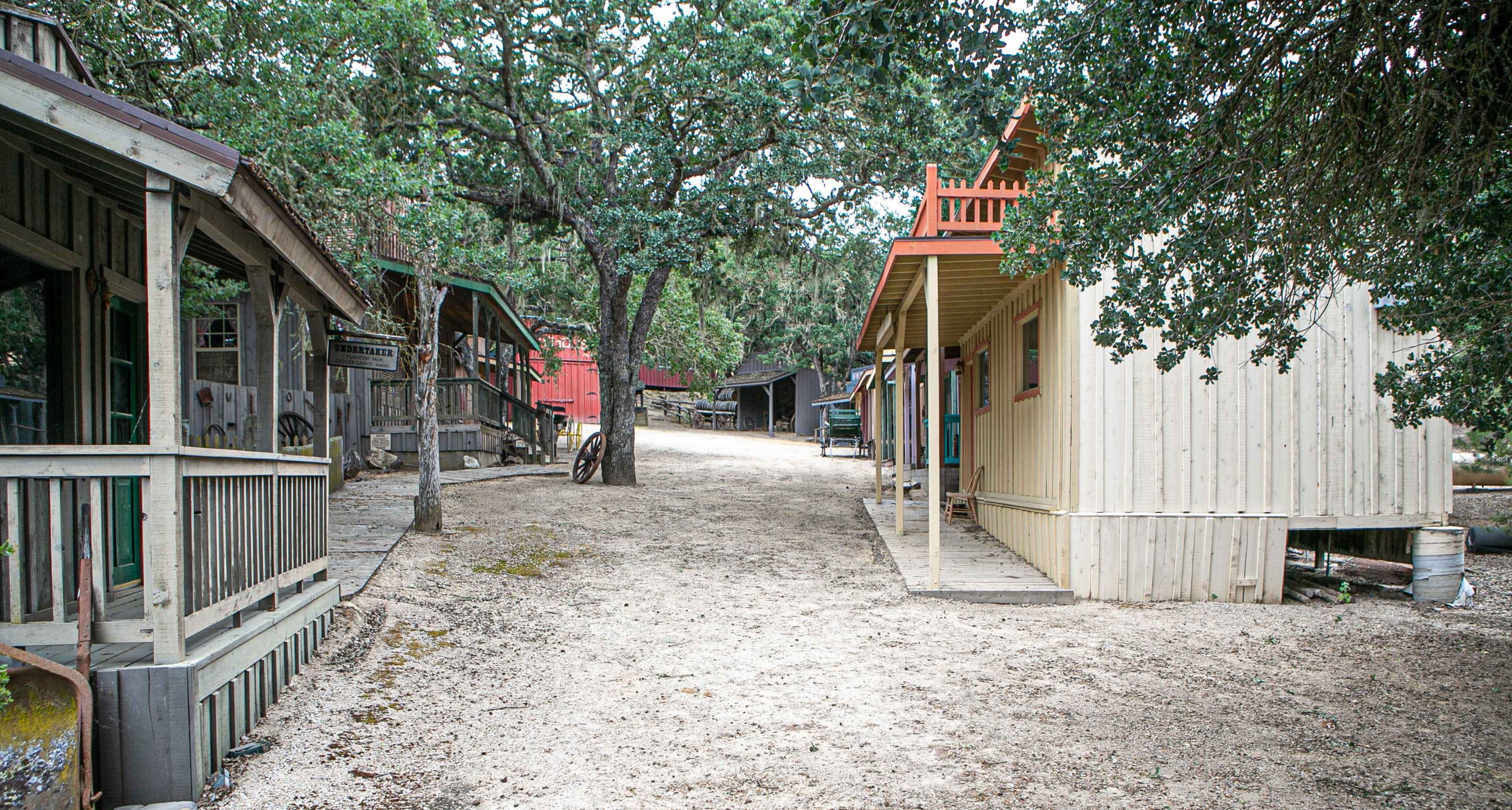 A dirt path winds through a cluster of rustic buildings surrounded by trees.