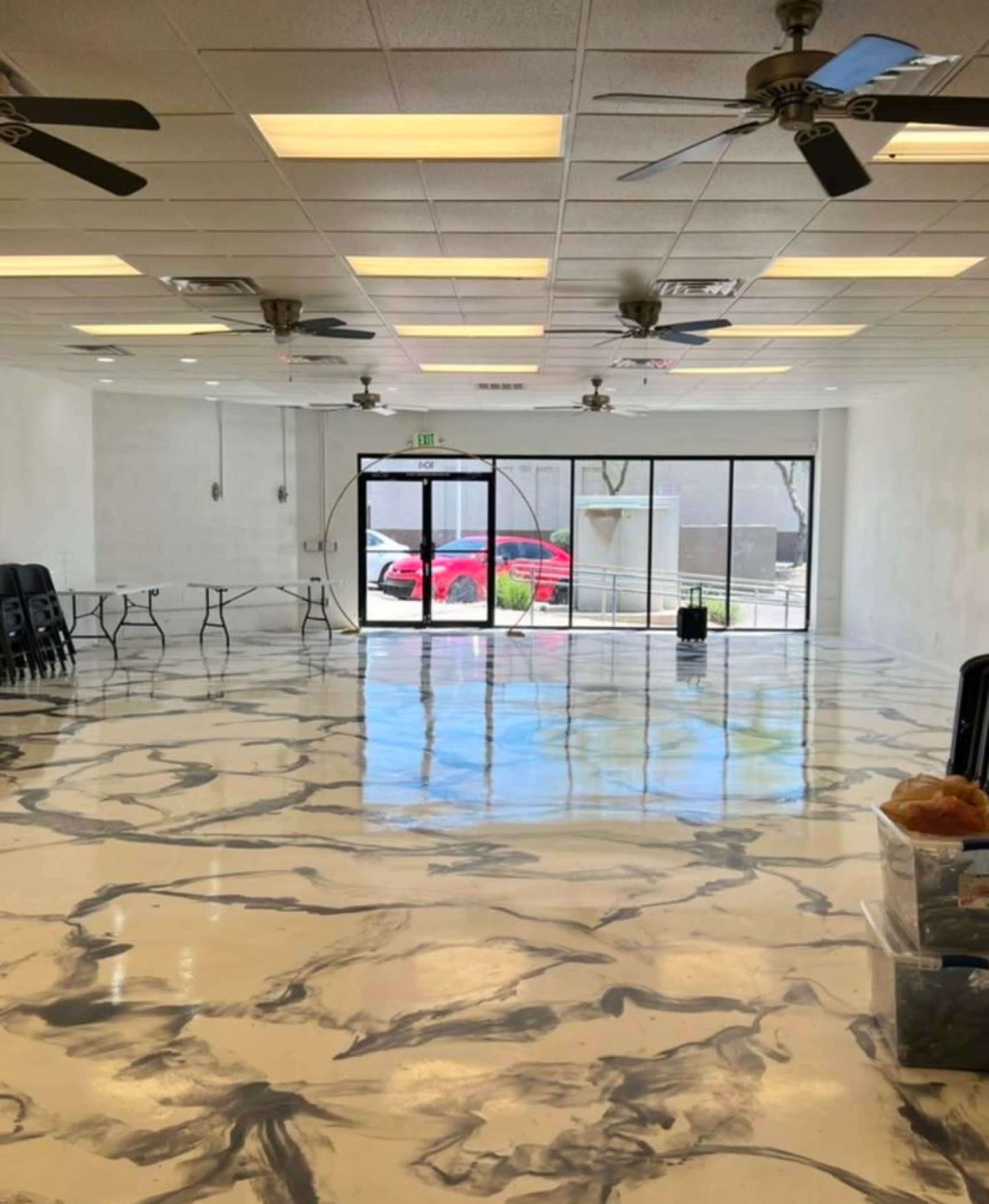 The image shows a spacious, empty room with a glossy, marbled floor, multiple ceiling fans, and large glass doors leading outside.