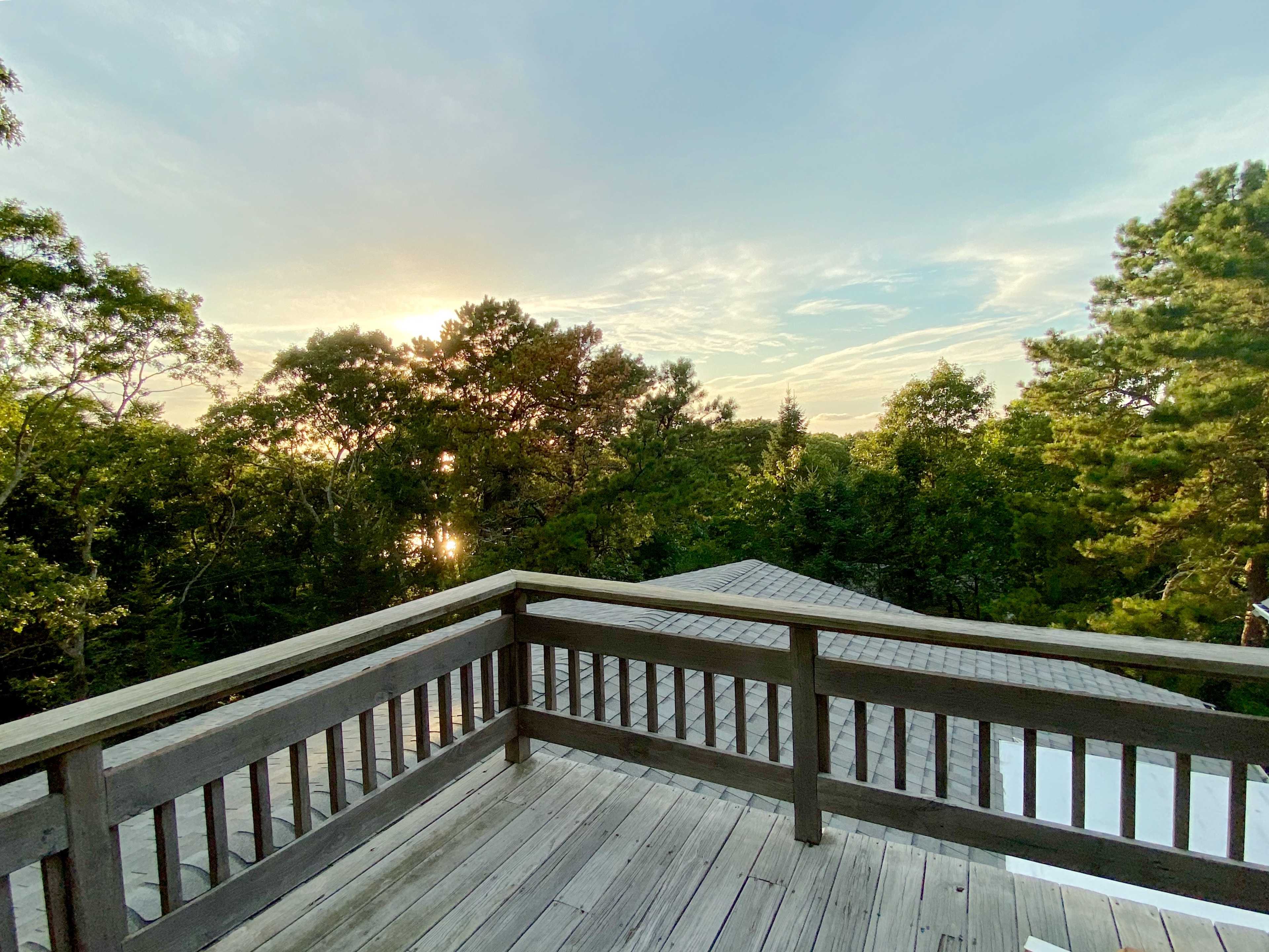 A wooden deck overlooking a wooded area with a view of a sunset in the background.