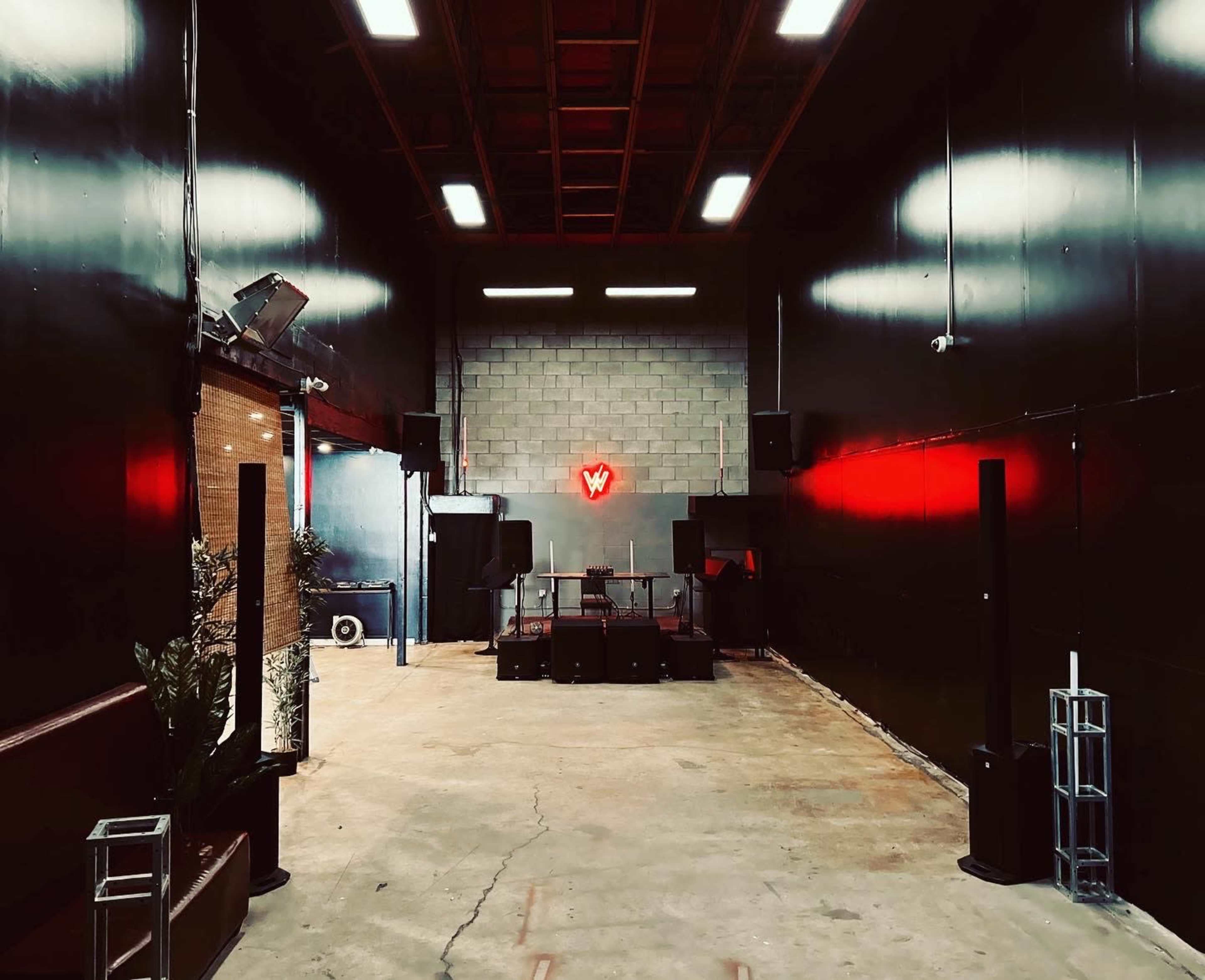 A spacious, industrial interior with black walls, a concrete floor, and a neon sign illuminated at the far end.