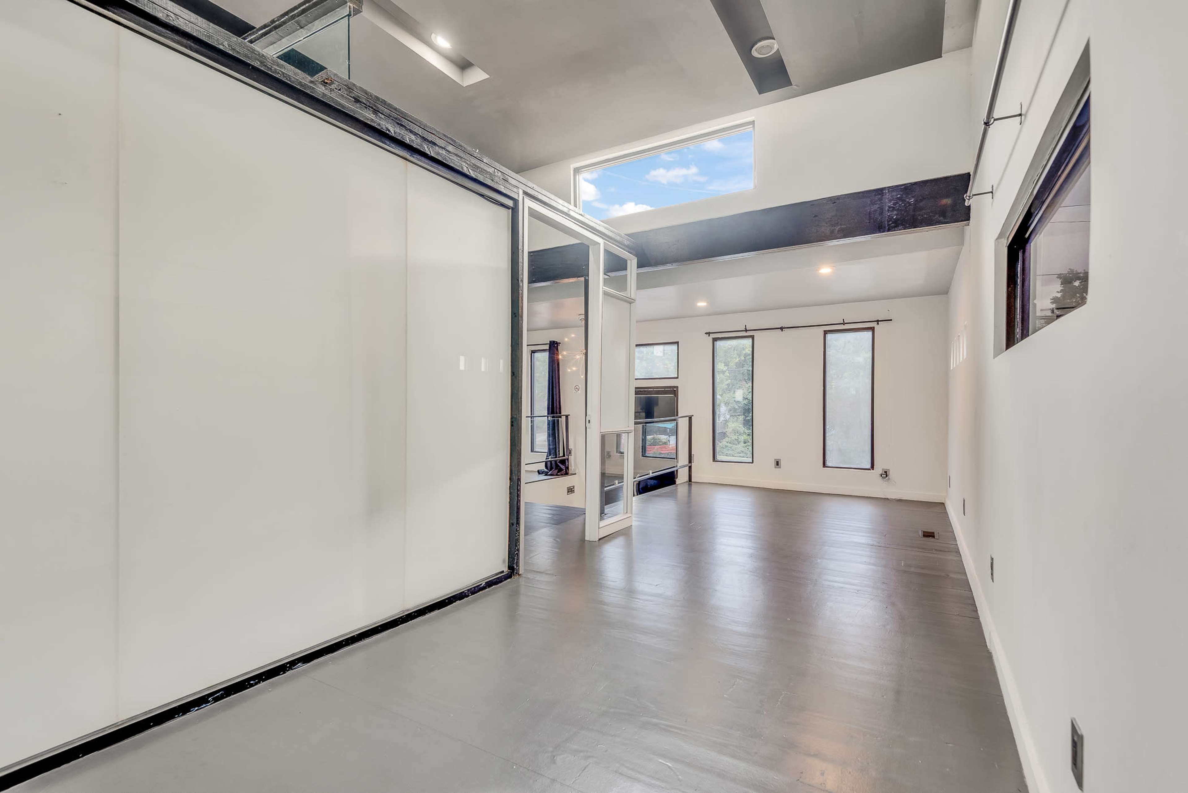 The image shows an empty, modern interior space with large windows and a sliding glass door leading to a balcony.