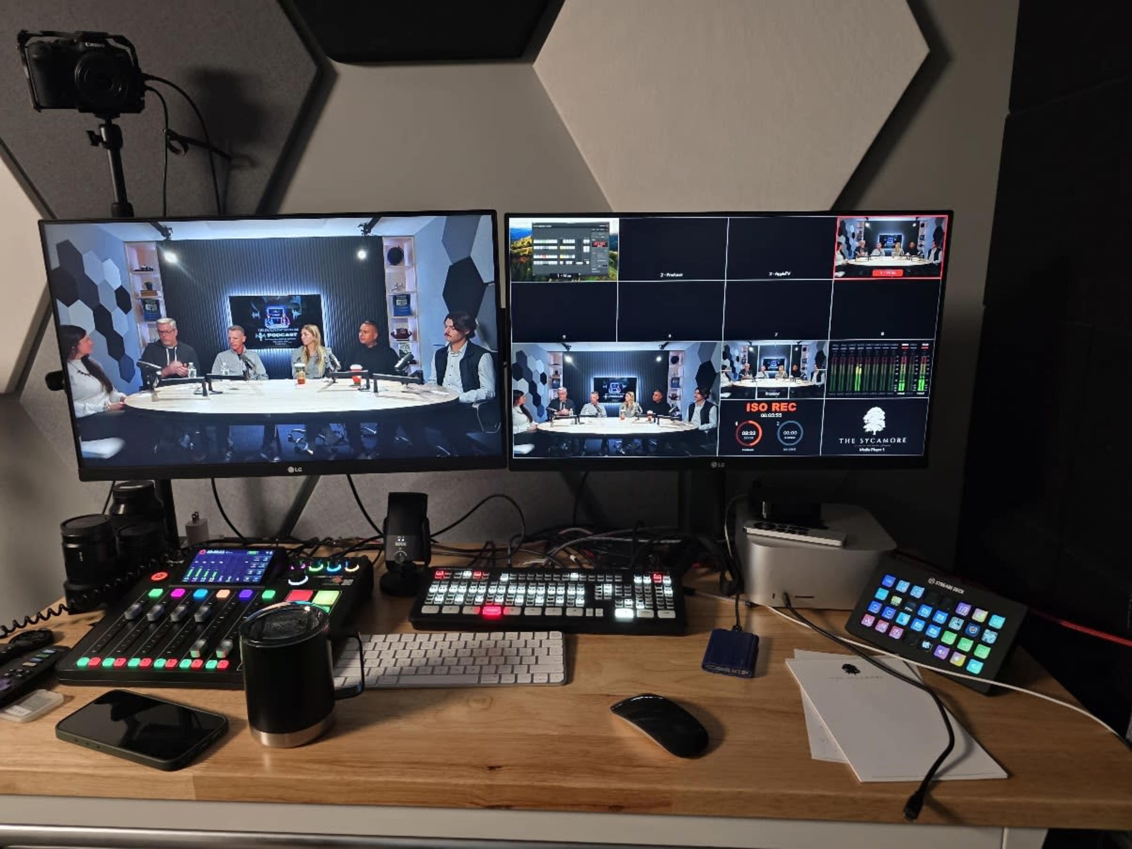 A modern video production setup features multiple monitors displaying live feed, controls, and a table of people engaged in discussion.
