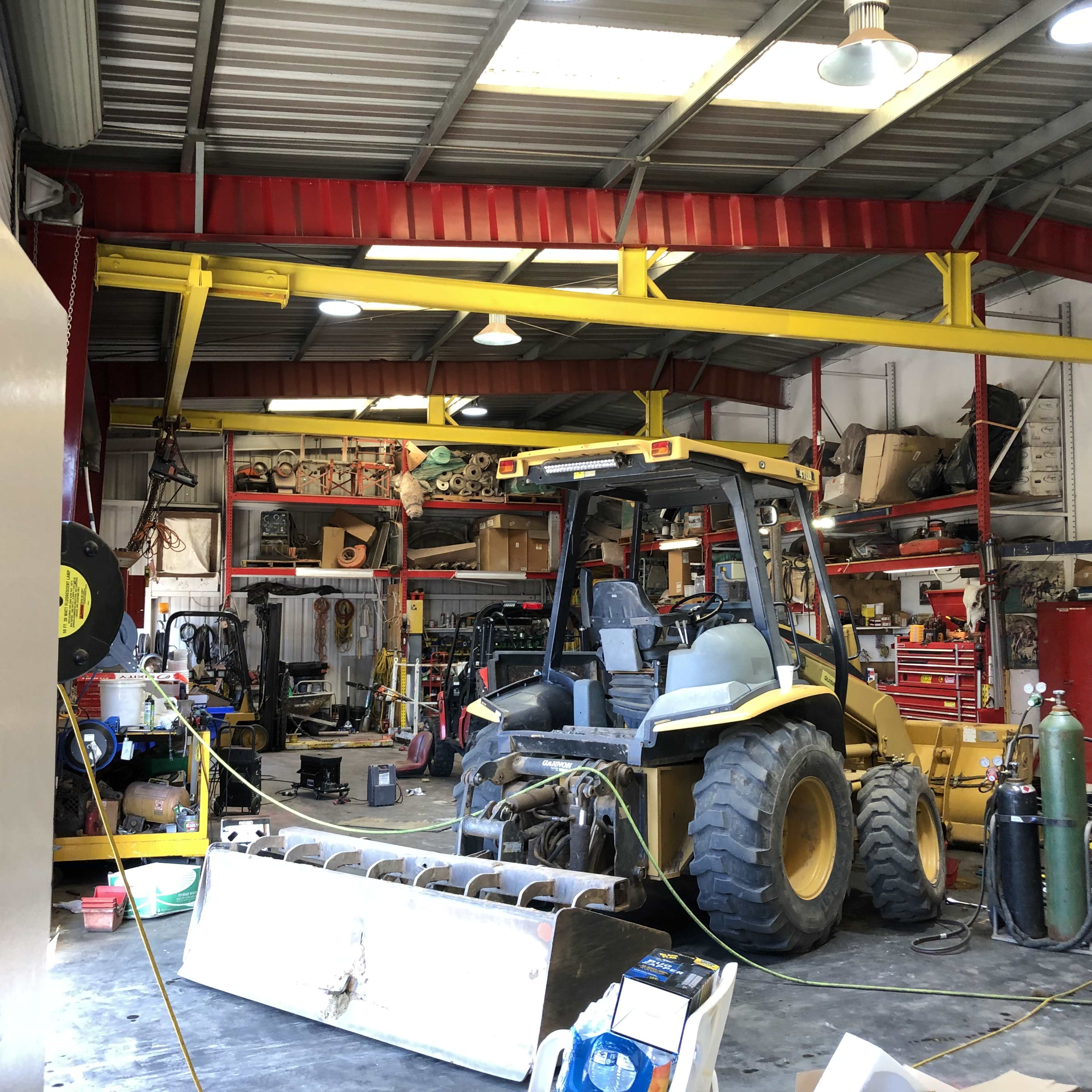 A yellow tractor with a front plow is parked inside a cluttered garage filled with various tools and equipment.