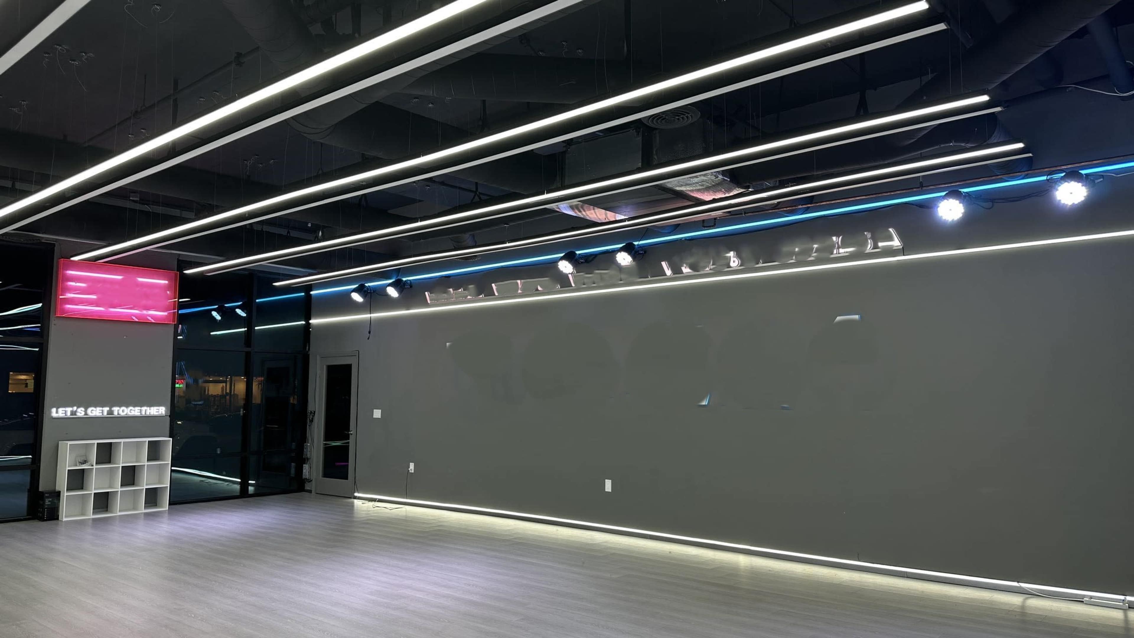 A modern, minimalist interior with a gray wall, ceiling lights, and a small shelf displaying the phrase "LET'S GET TOGETHER."