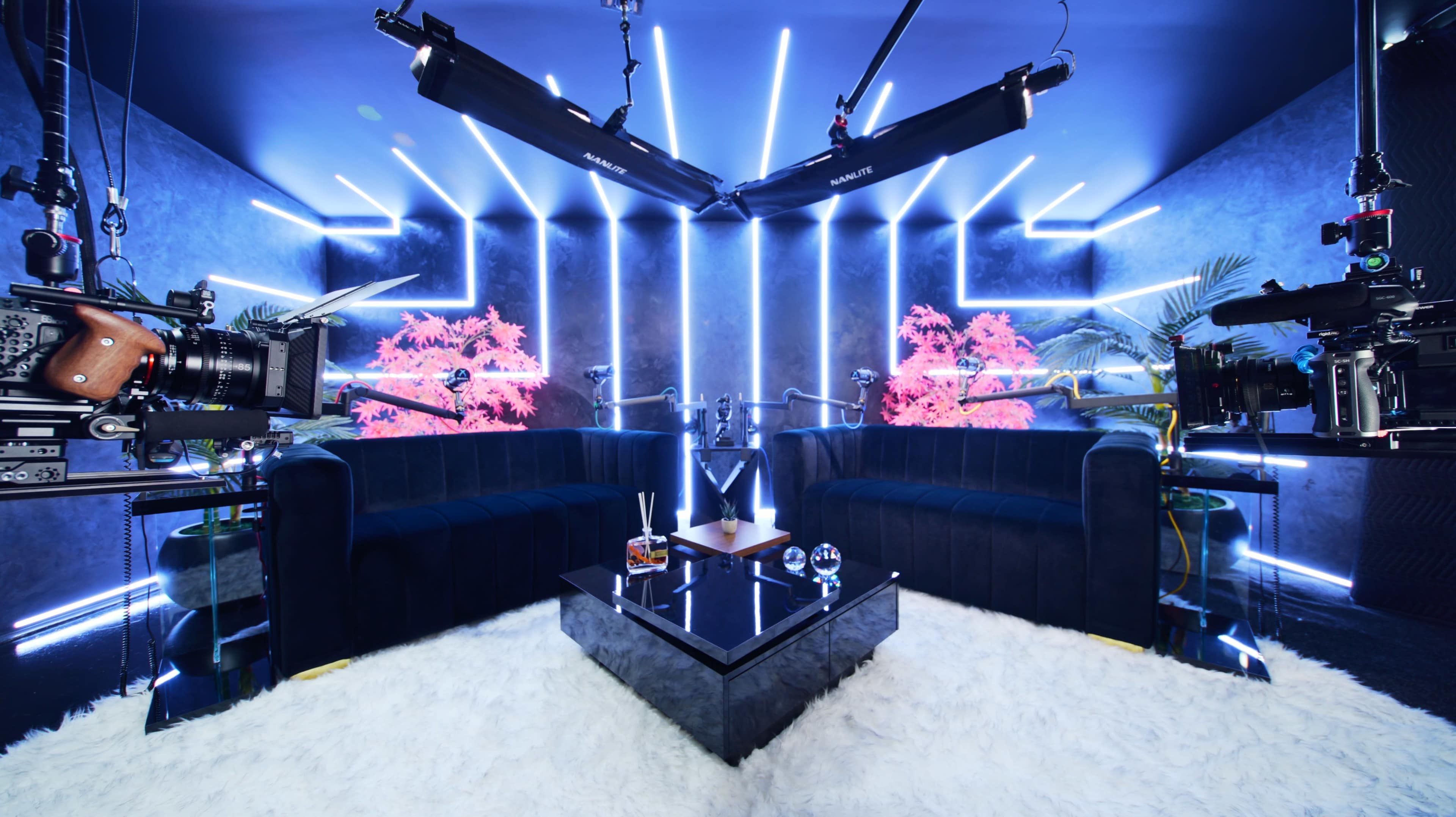 A modern studio setup features two sofas facing each other, a glass coffee table, and neon lights illuminating the space.