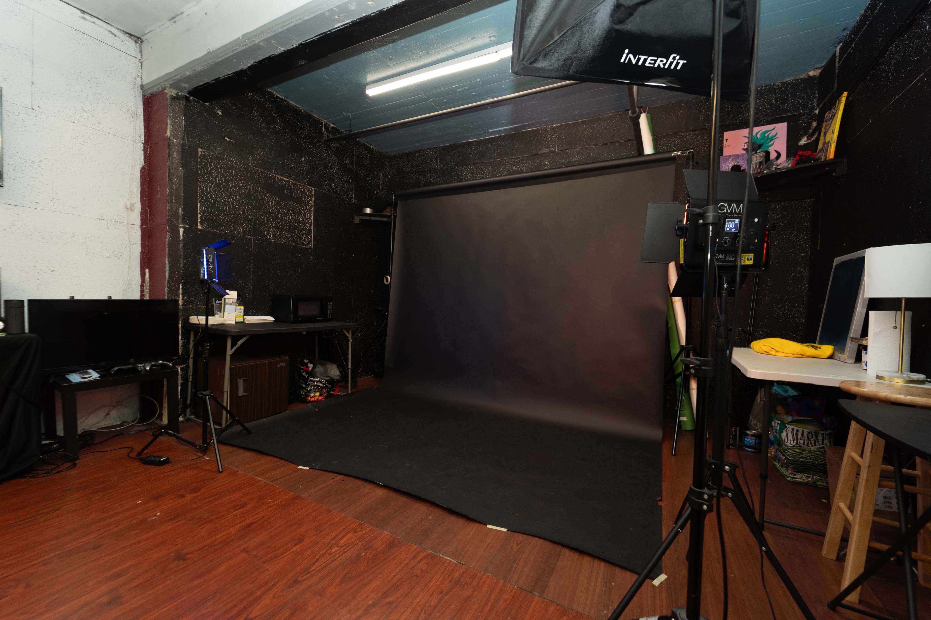 The image shows a photography studio with a black backdrop, lighting equipment, and various accessories scattered around the room.