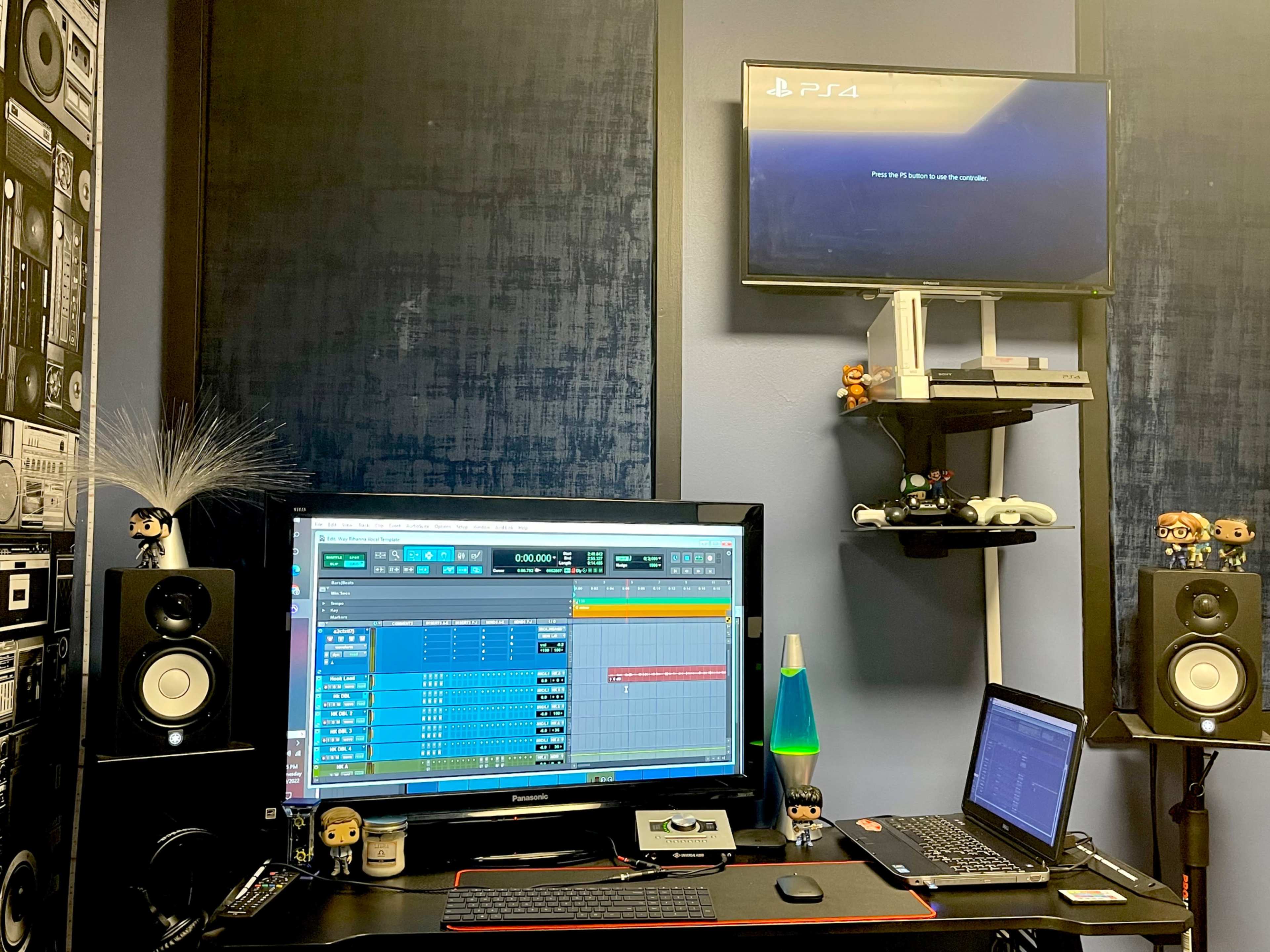 A recording studio setup features a large monitor displaying music software, a laptop, speakers, and a television showing a PlayStation 4 screen.